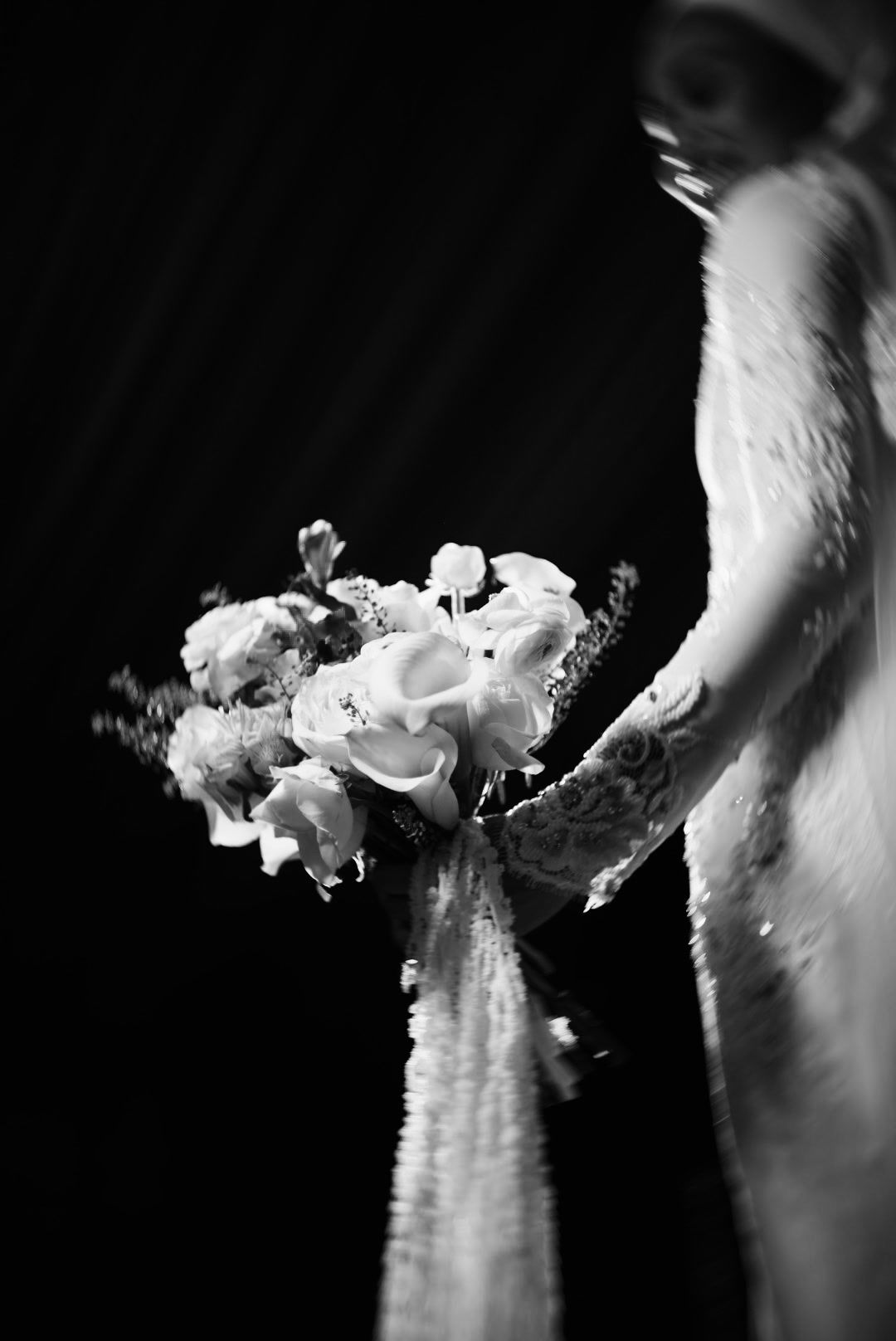 Black and white artistic shot of bride holding elegant floral wedding bouquet in lace gown.