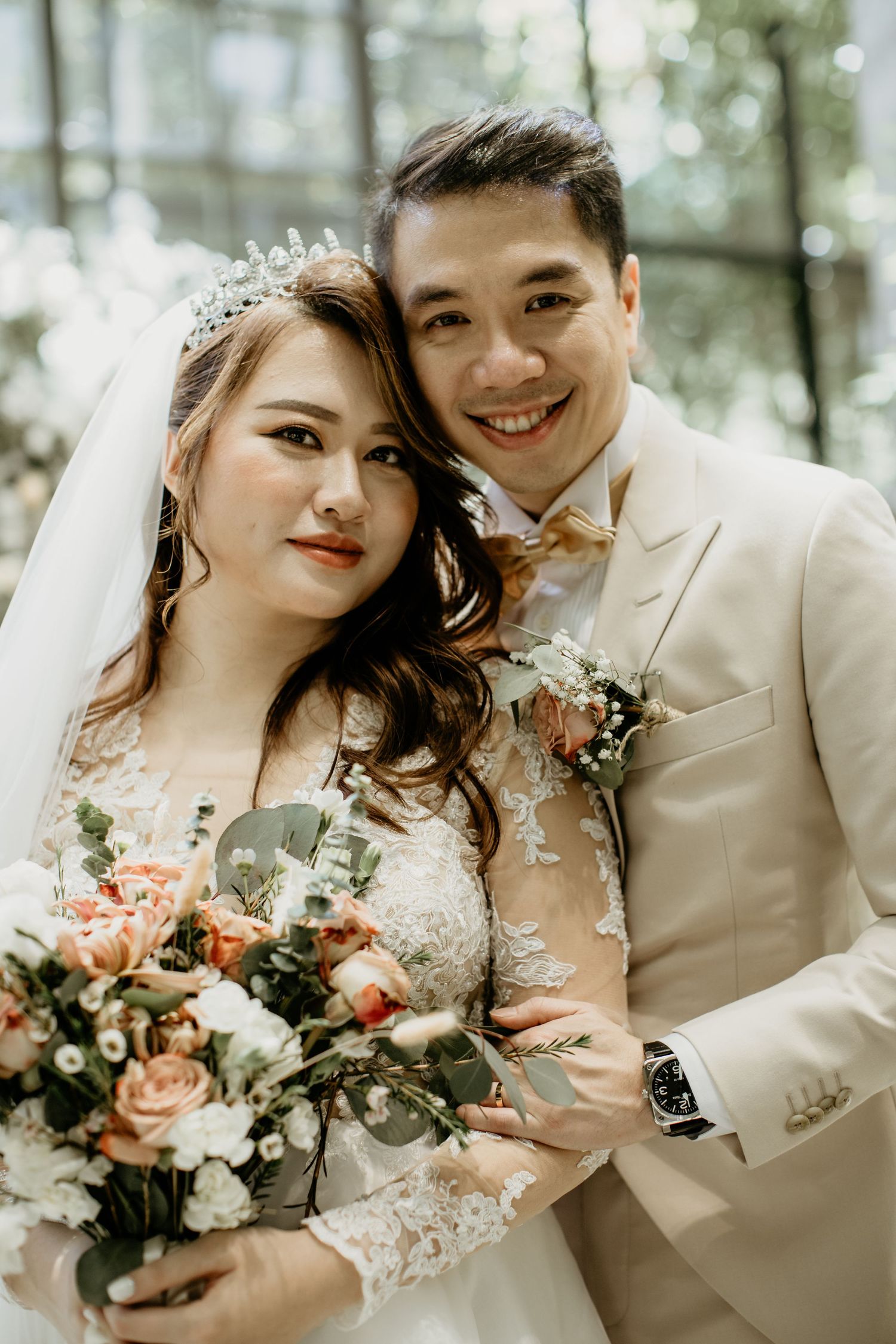 Bride and groom pose together smiling, bride holding a bouquet of peach and white roses.