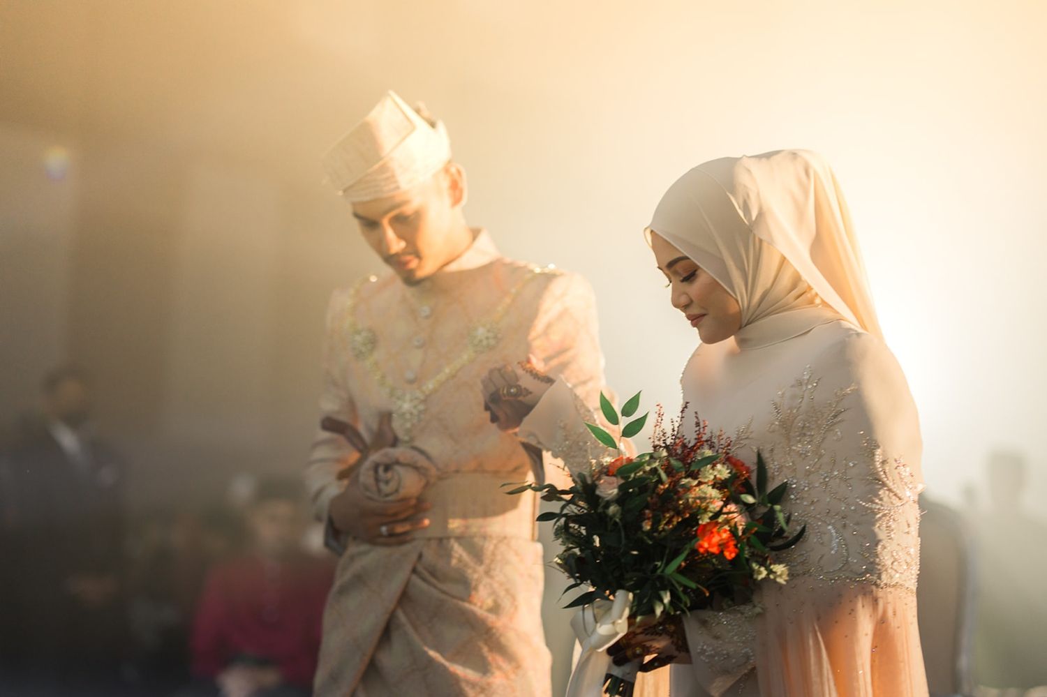 Malaysian  couple in cream wedding attire, bride holding colorful bouquet during traditional Nikah ceremony in golden light. MK K Clique