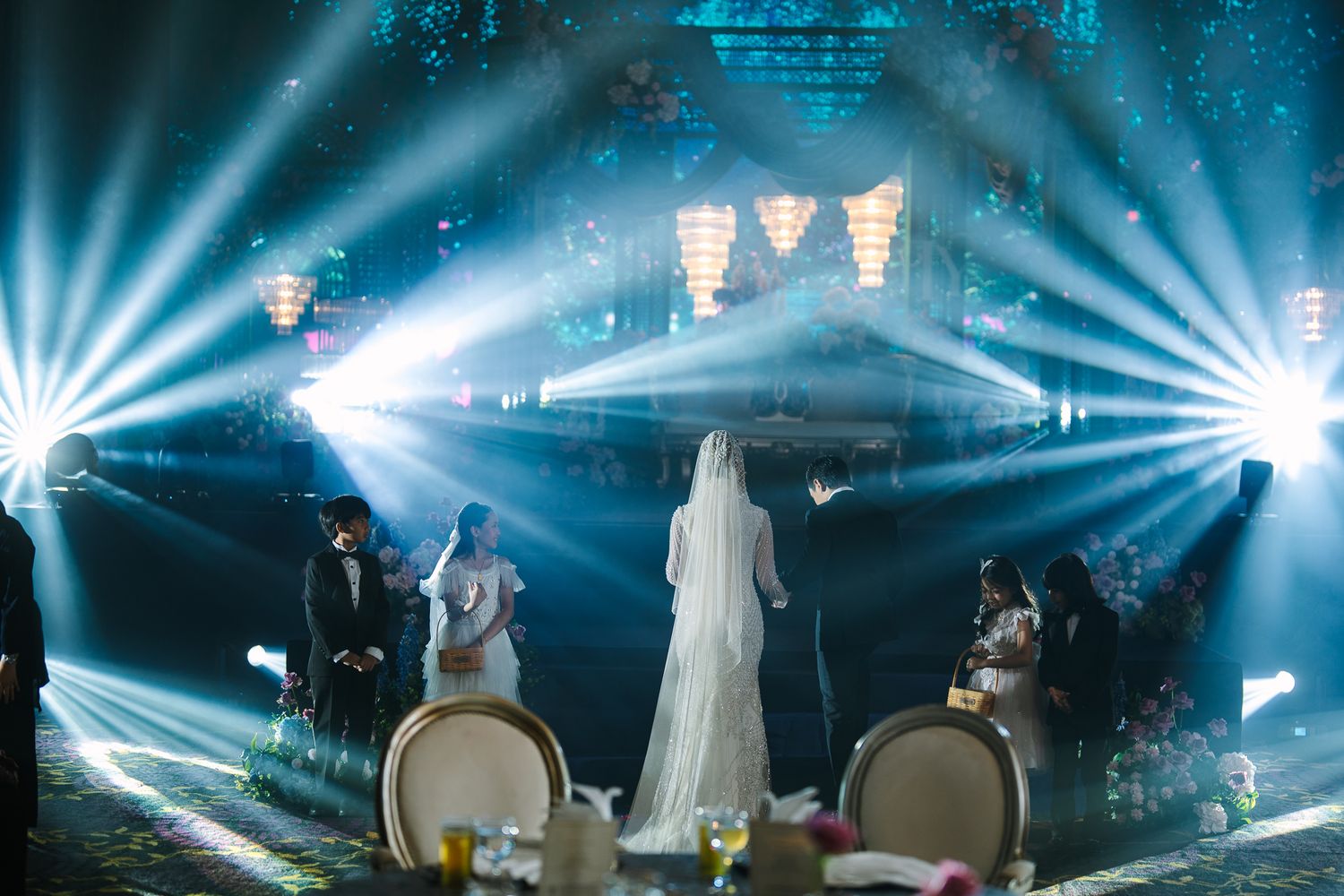 Bride and groom silhouetted by dramatic blue stage lights at elegant wedding reception venue.