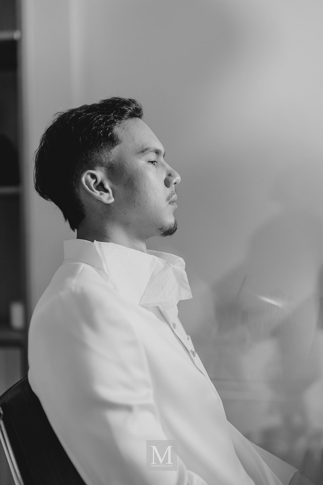 Black and white portrait of a young man in a white shirt seated and looking upward thoughtfully.