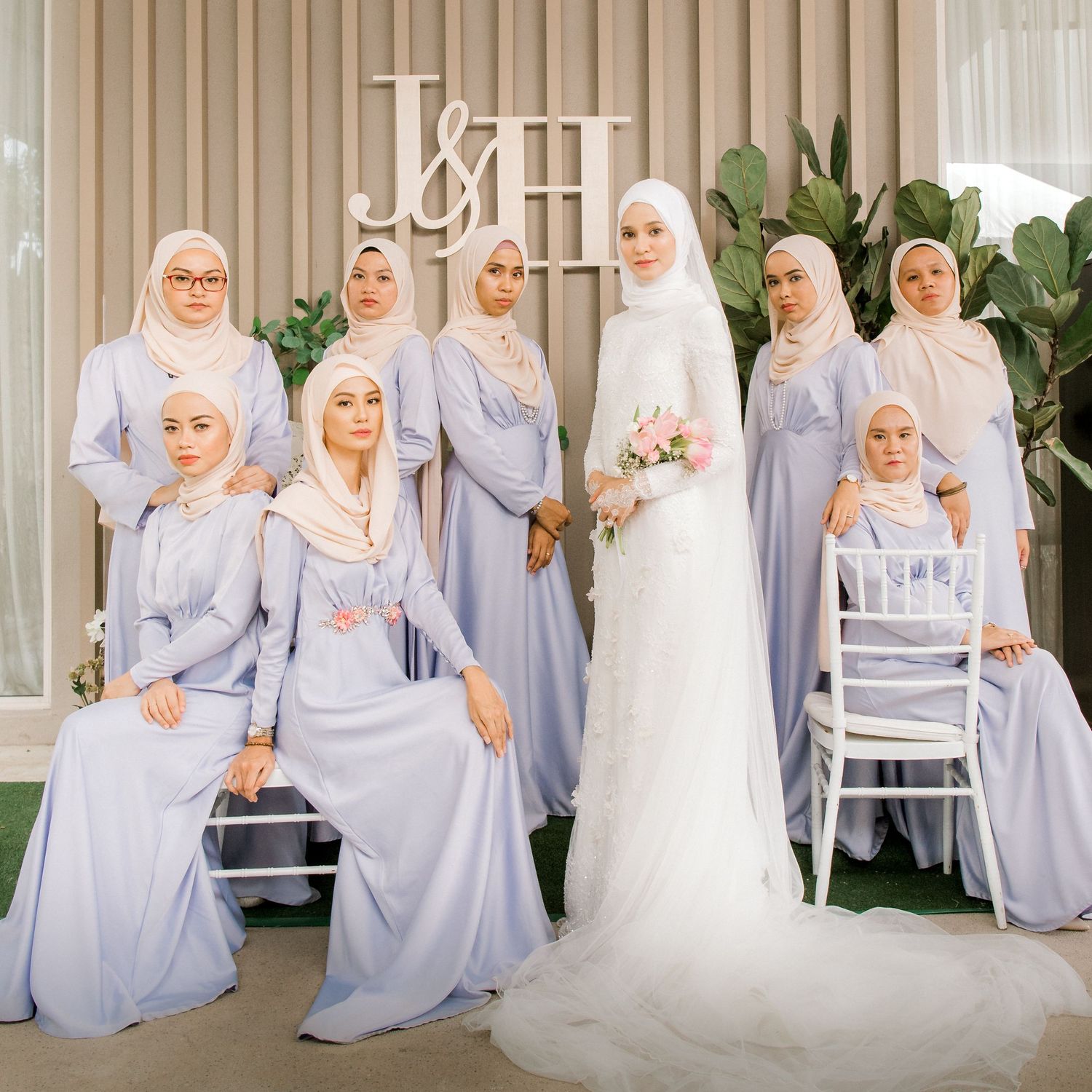 Malaysian bride in white hijab gown poses with bridesmaids in lavender dresses at elegant wedding ceremony.