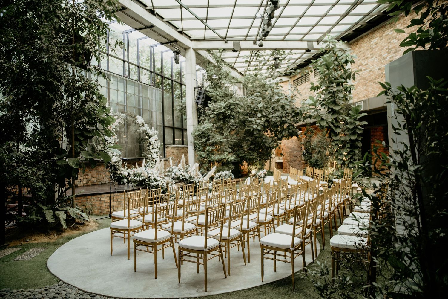 Stunning greenhouse wedding ceremony venue with rows of gold Chiavari chairs surrounded by lush tropical greenery.