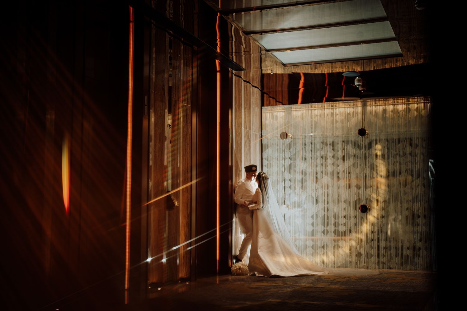 Romantic wedding couple sharing intimate moment in dramatic architectural space with flowing bridal gown train.
