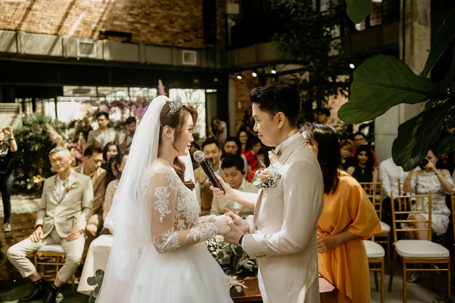 Bride and groom exchange vows during an indoor wedding ceremony with guests seated in the background.