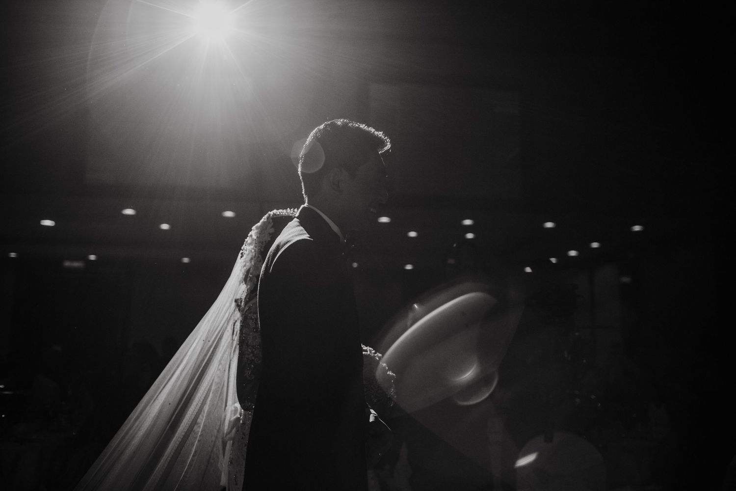 Black and white silhouette of bride and groom sharing a romantic moment, with dramatic backlighting at wedding reception.