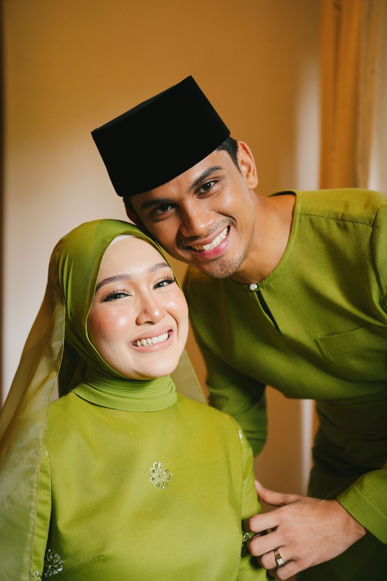 Smiling Malaysian couple in matching green traditional Baju Kurung and Baju Melayu wedding attire.