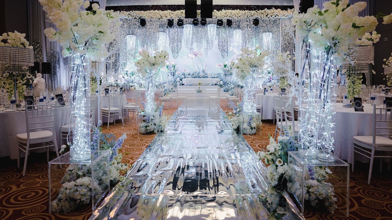 Luxurious wedding venue with illuminated crystal aisle, white orchids, and fairy lights.