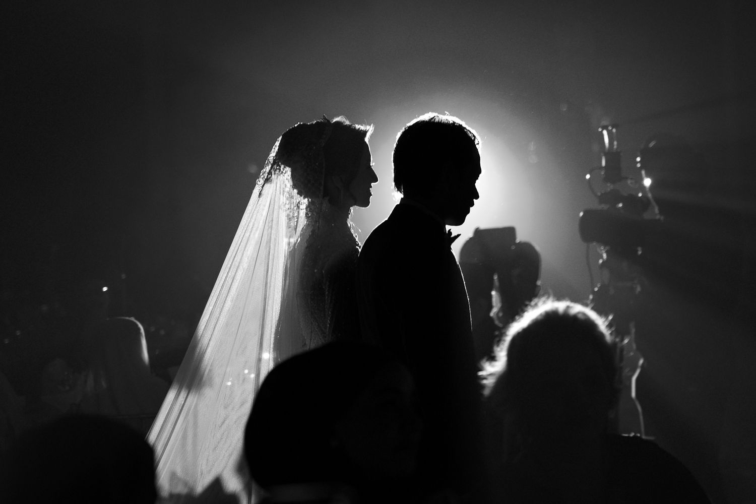 Black and white silhouette of bride and groom at their wedding ceremony with dramatic backlight.
