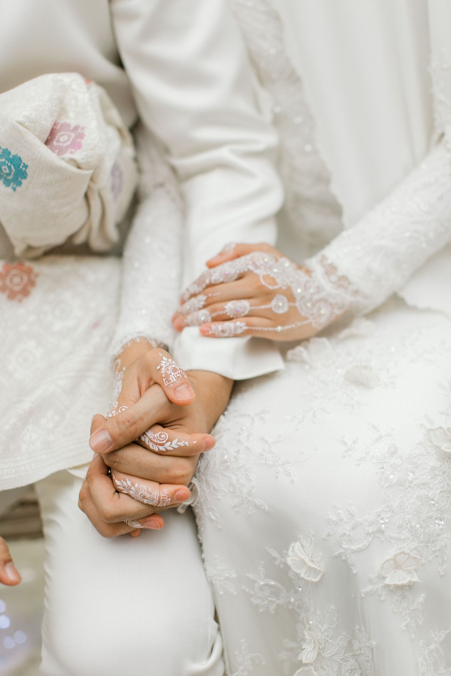 Close-up of bride and groom holding hands with intricate white henna bridal mehndi design.