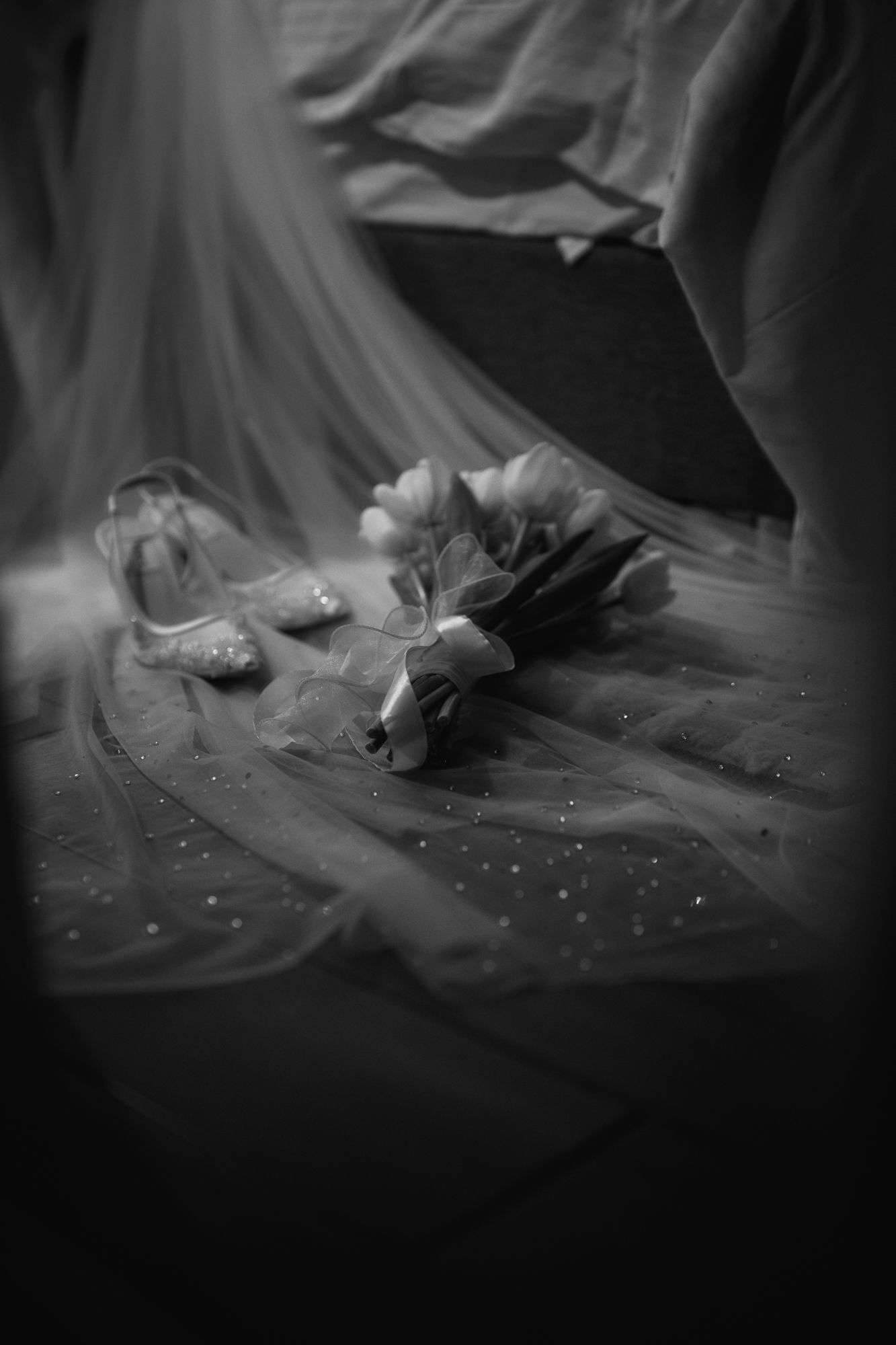 Black and white close-up of a bridal veil with floral bouquet and wedding accessories on fabric.