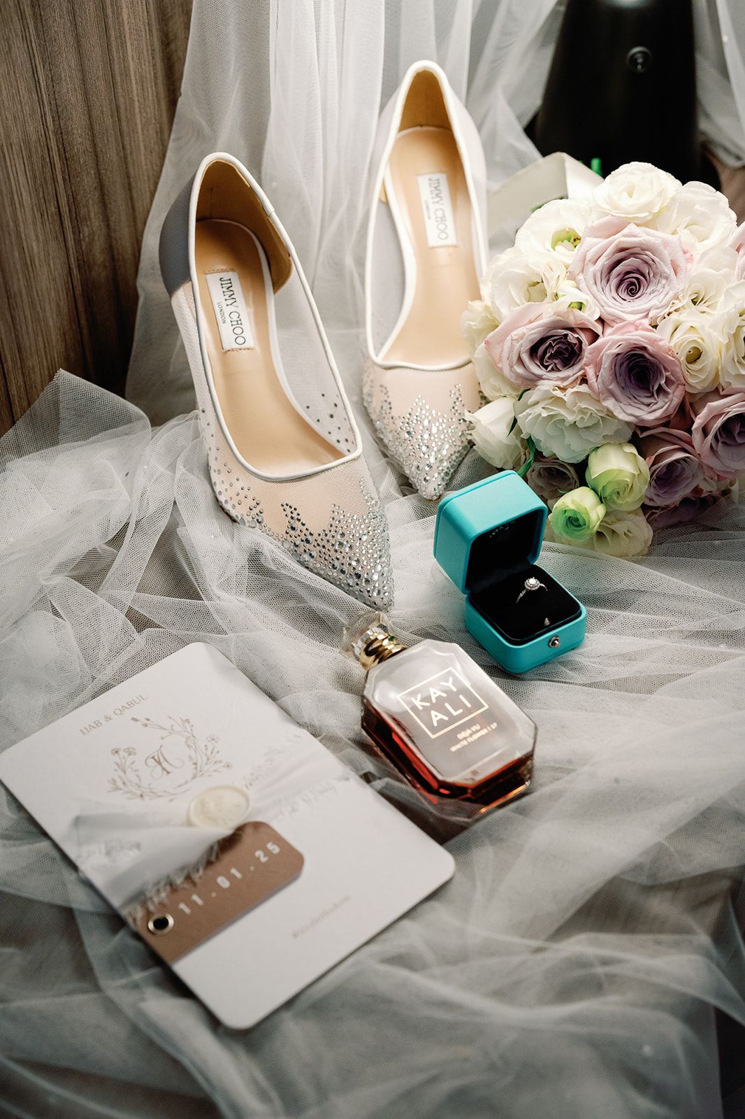 Wedding flat lay featuring Jimmy Choo heels, engagement ring, perfume, bouquet, and invitation.