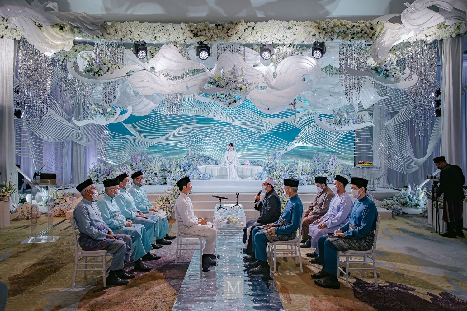 An elegant Malay wedding ceremony with guests seated in a stunning blue and white decorated hall.