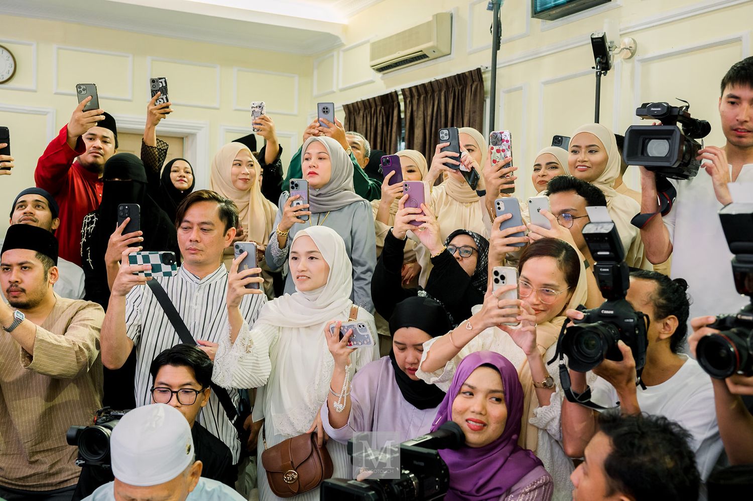 Excited wedding guests taking photos with smartphones during a lively Malaysian wedding celebration.