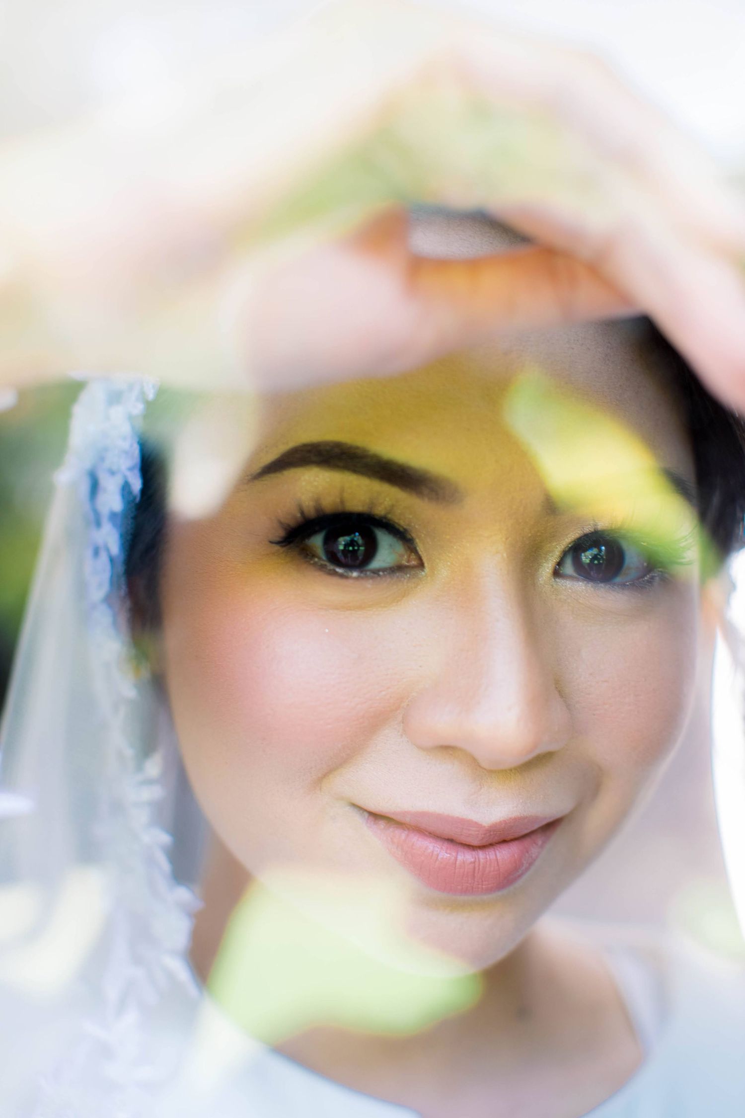 Close-up portrait of beautiful Asian bride in lace veil with soft natural lighting.