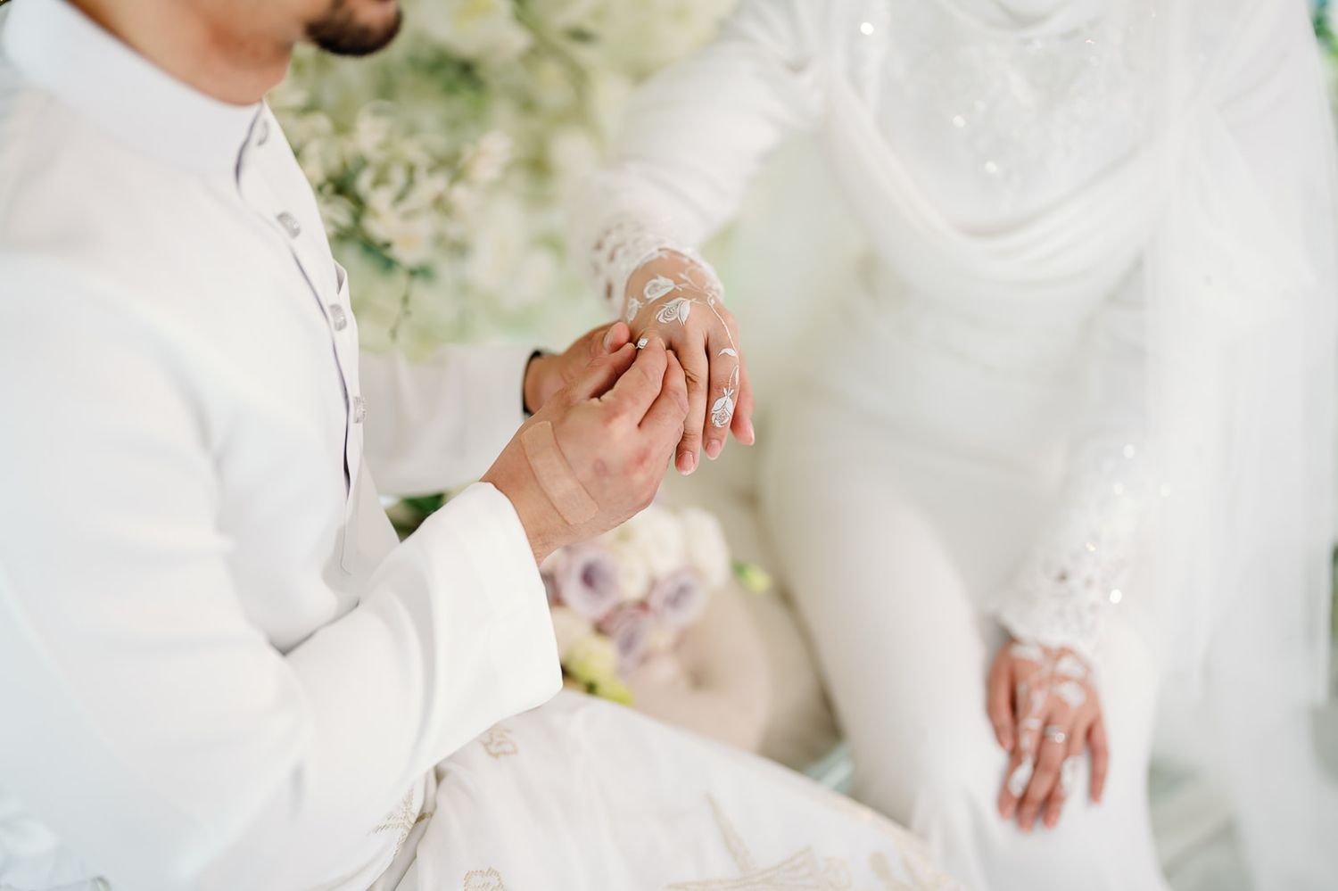 Malaysian  groom placing a wedding ring on his bride's finger during an Islamic wedding ceremony.