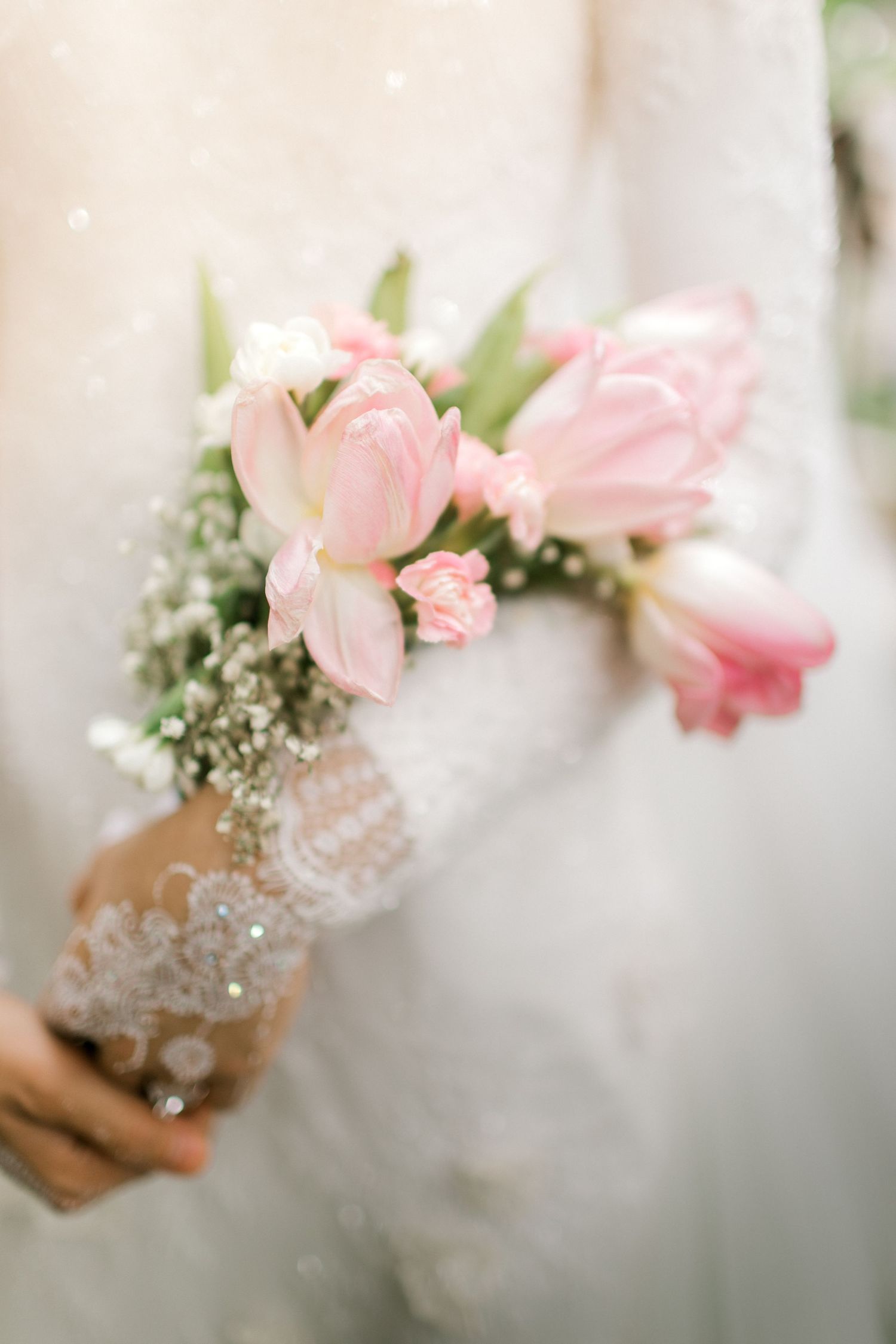 Bride holding a delicate bouquet of pink tulips and baby's breath, wearing a lace wedding dress.