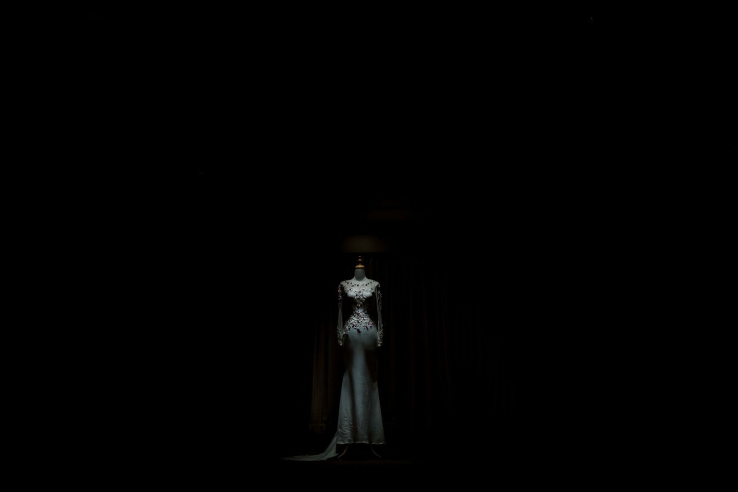 A solitary figure in a white gown stands dramatically illuminated against a dark, mysterious background.