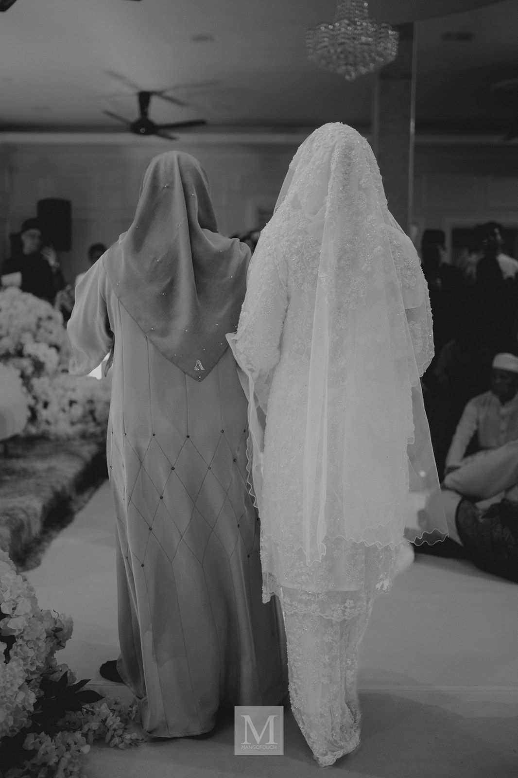Black and white photo of two women in hijab walking together at a Malaysian wedding ceremony.