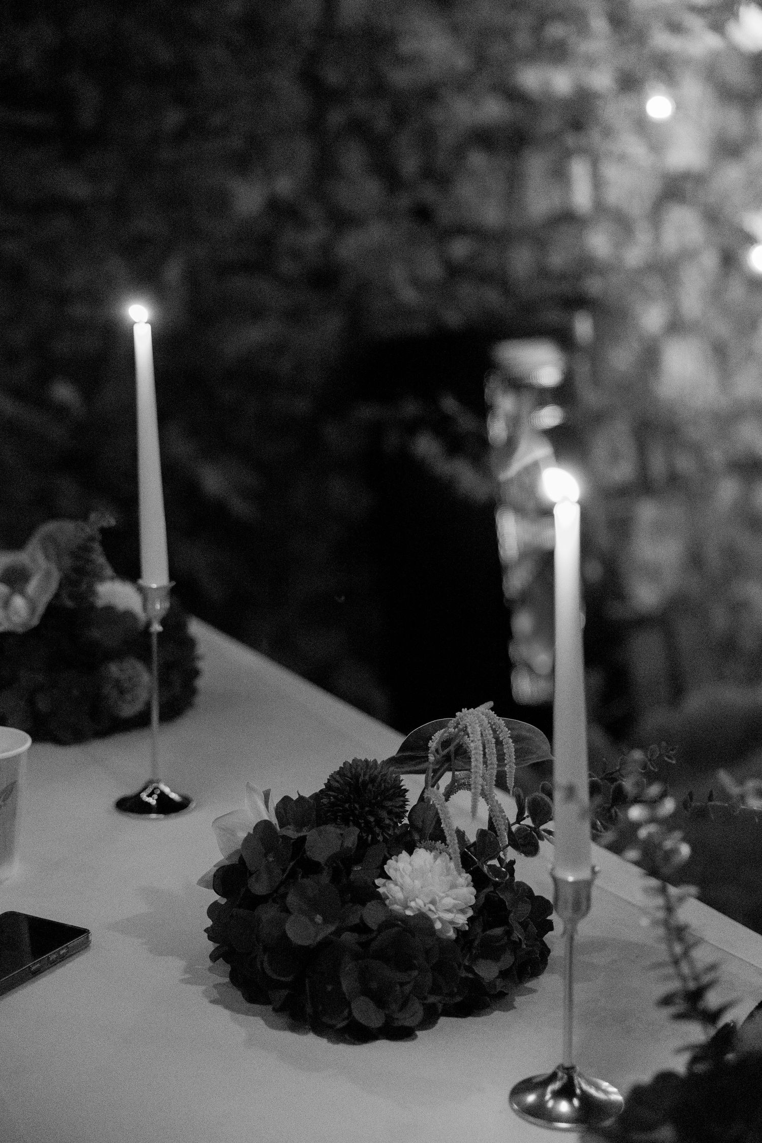 Black and white photo of elegant wedding table with candles and floral centerpiece at evening outdoor reception.