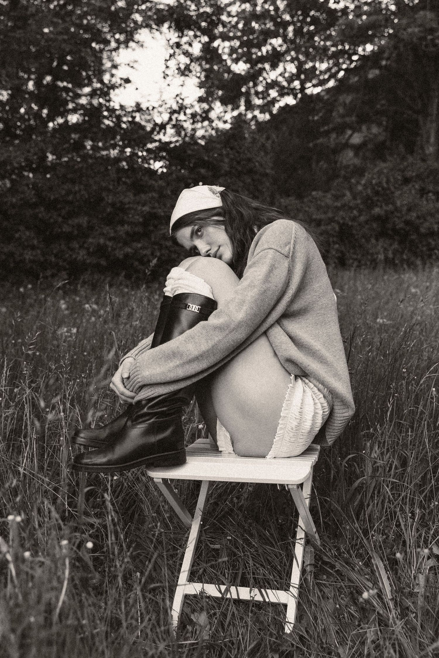 Vintage sepia photo of woman in grey sweater hugging boot on chair in meadow.