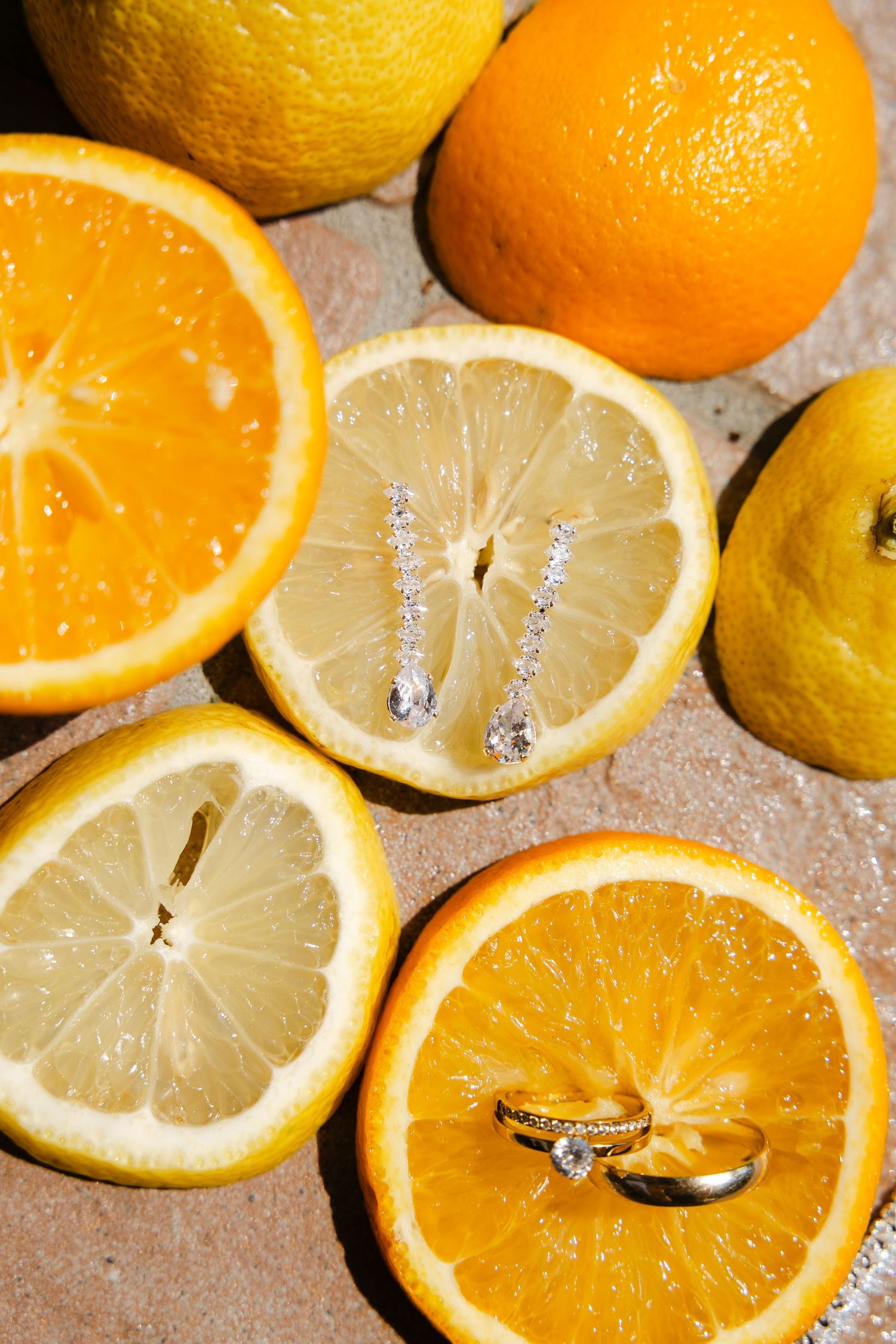 Wedding rings and diamond earrings displayed on sliced oranges and lemons for a citrus-themed bridal jewelry flat lay.