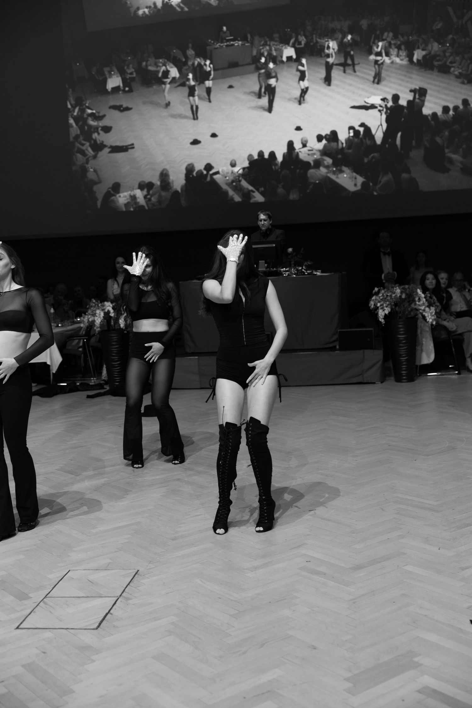 Black and white photo of female dancers performing in thigh-high boots at a formal event or gala.