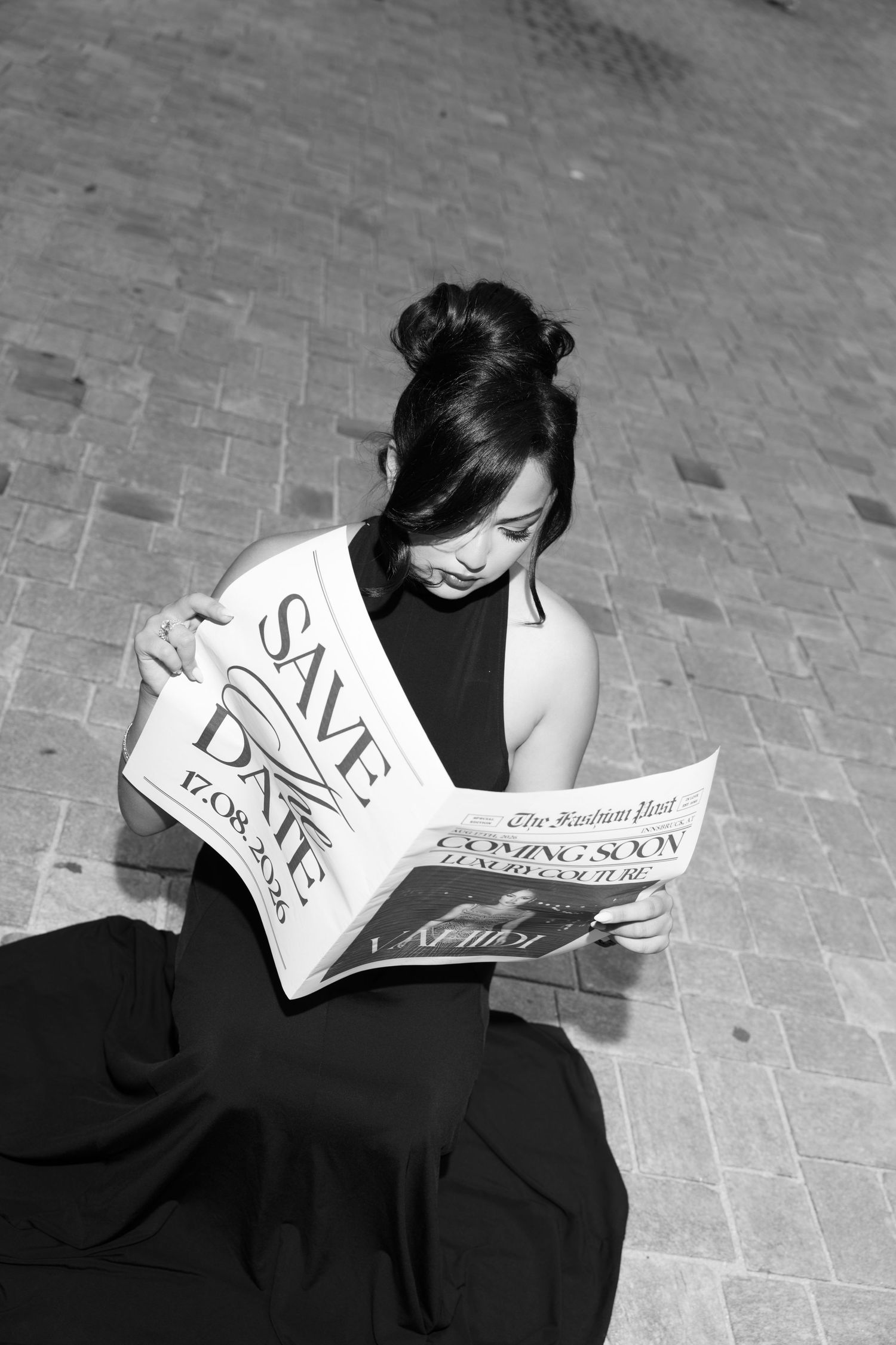 Black and white photo of woman in black dress reading Save the Date newspaper.