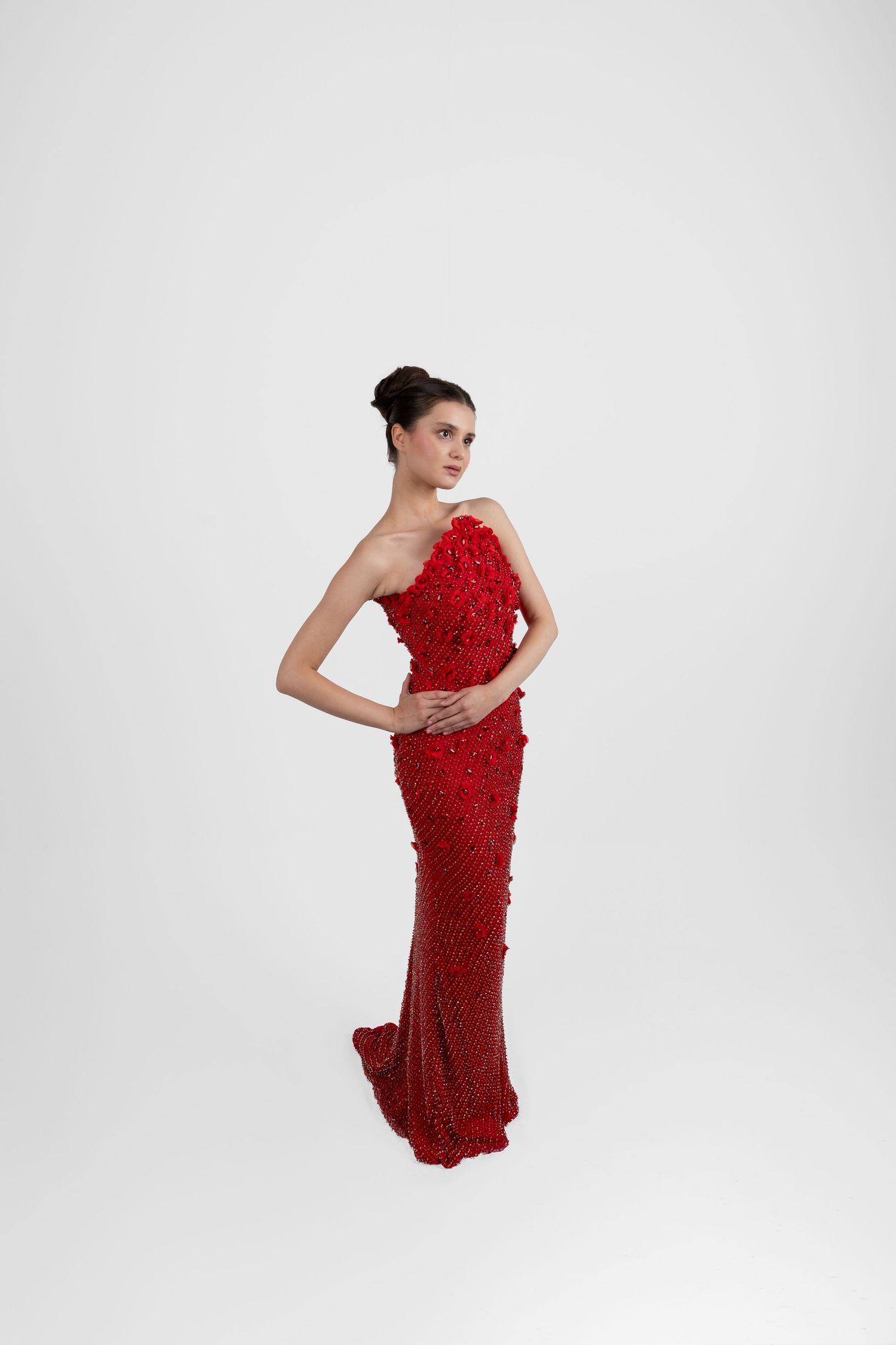 Model wearing a stunning red one-shoulder gown with floral embellishments and sequin details on white background.