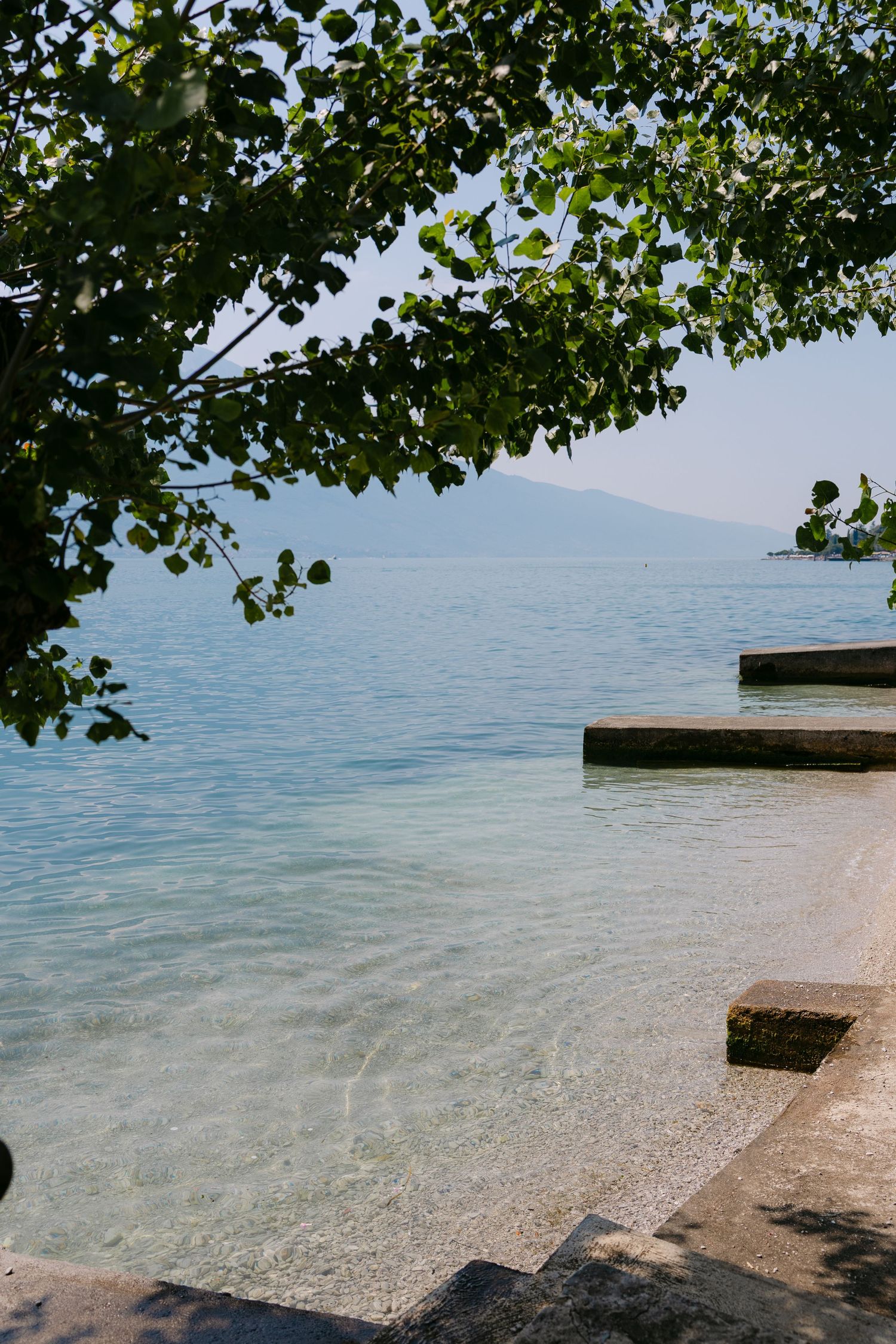 Serene lakeside view with crystal clear turquoise water, stone steps, and mountain backdrop on sunny day.