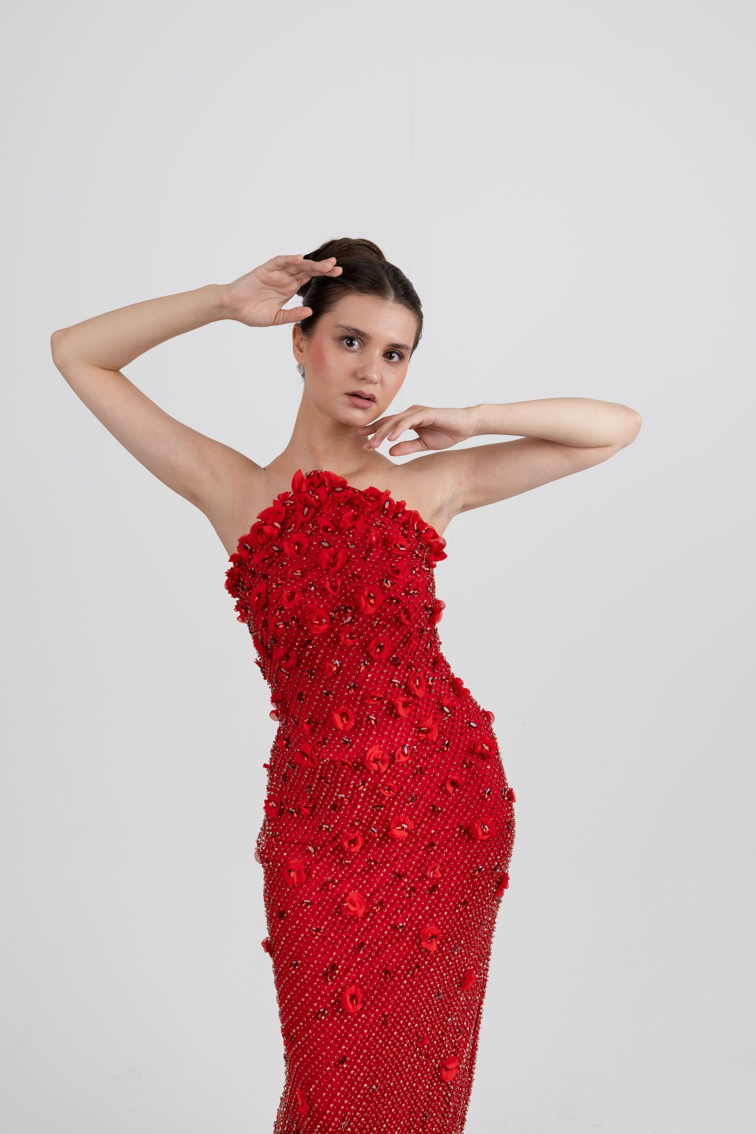 Woman posing in a strapless red beaded gown with floral embellishments against a white background.