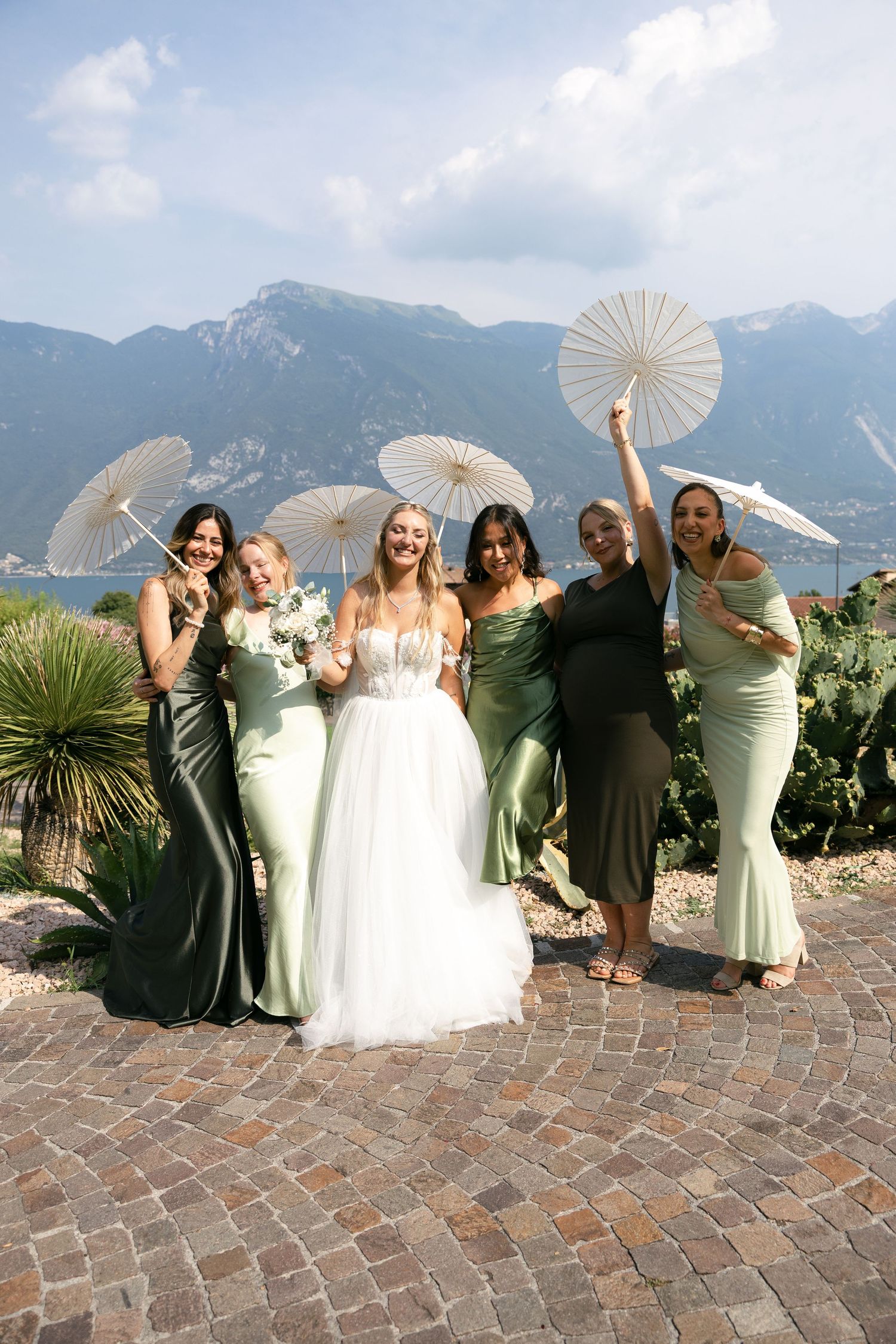 Bride in white gown poses with four bridesmaids in green dresses holding parasols with mountain backdrop.