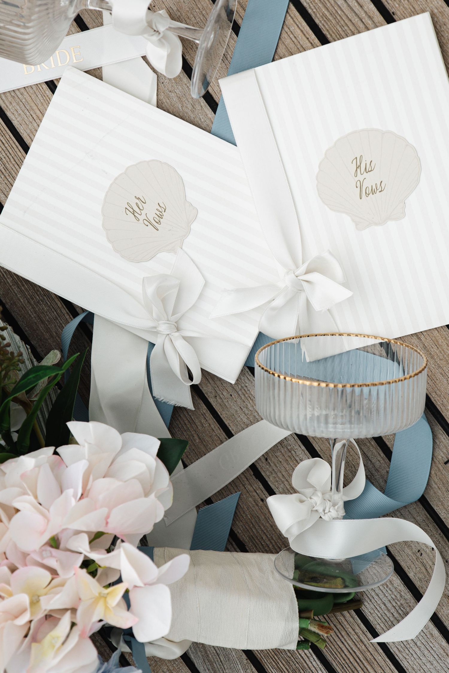 Elegant wedding vow books with white ribbon bows, blue satin ribbons, and pink flowers on a wooden surface.