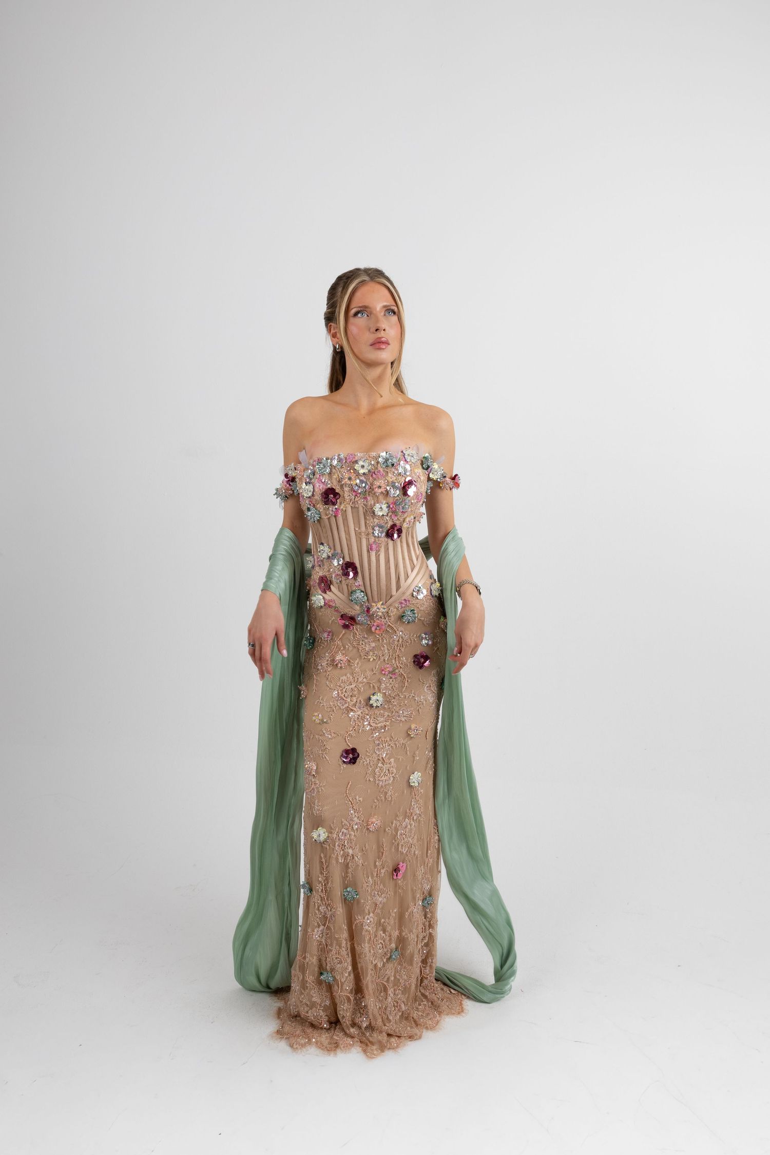 Woman in elegant floral embellished off-shoulder gown with green chiffon sleeves and beaded lace skirt.