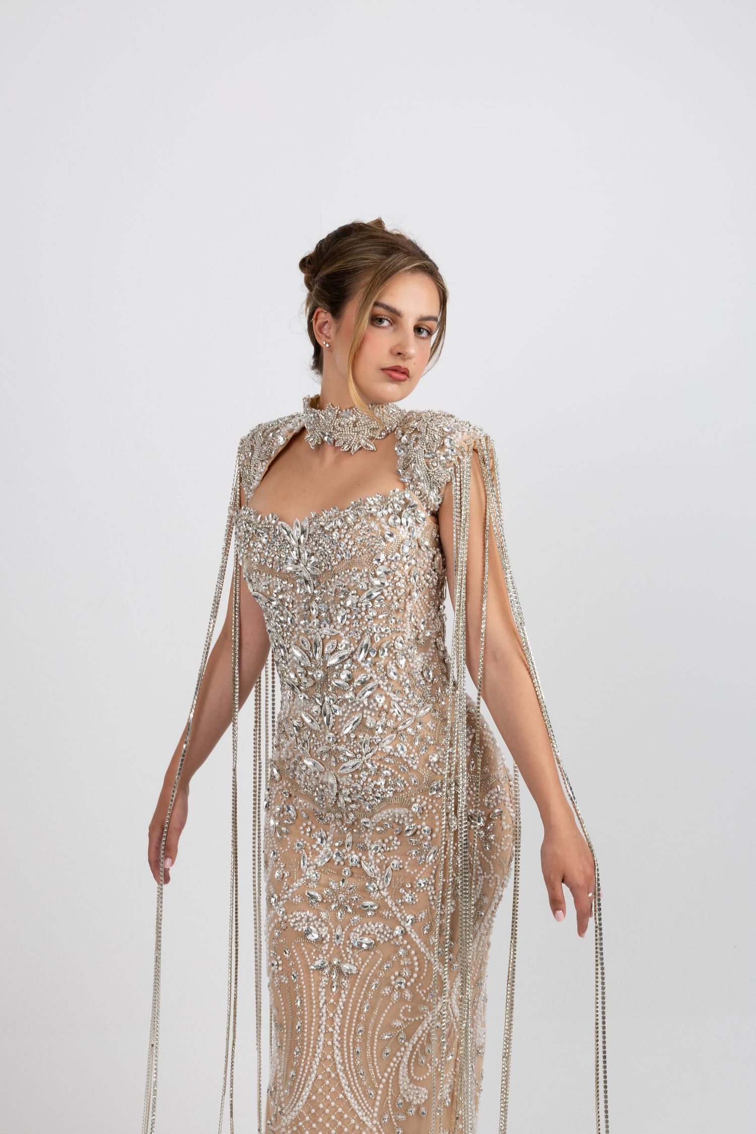 Elegant beaded silver gown with fringe cape overlay and intricate crystal embellishments on a female model.