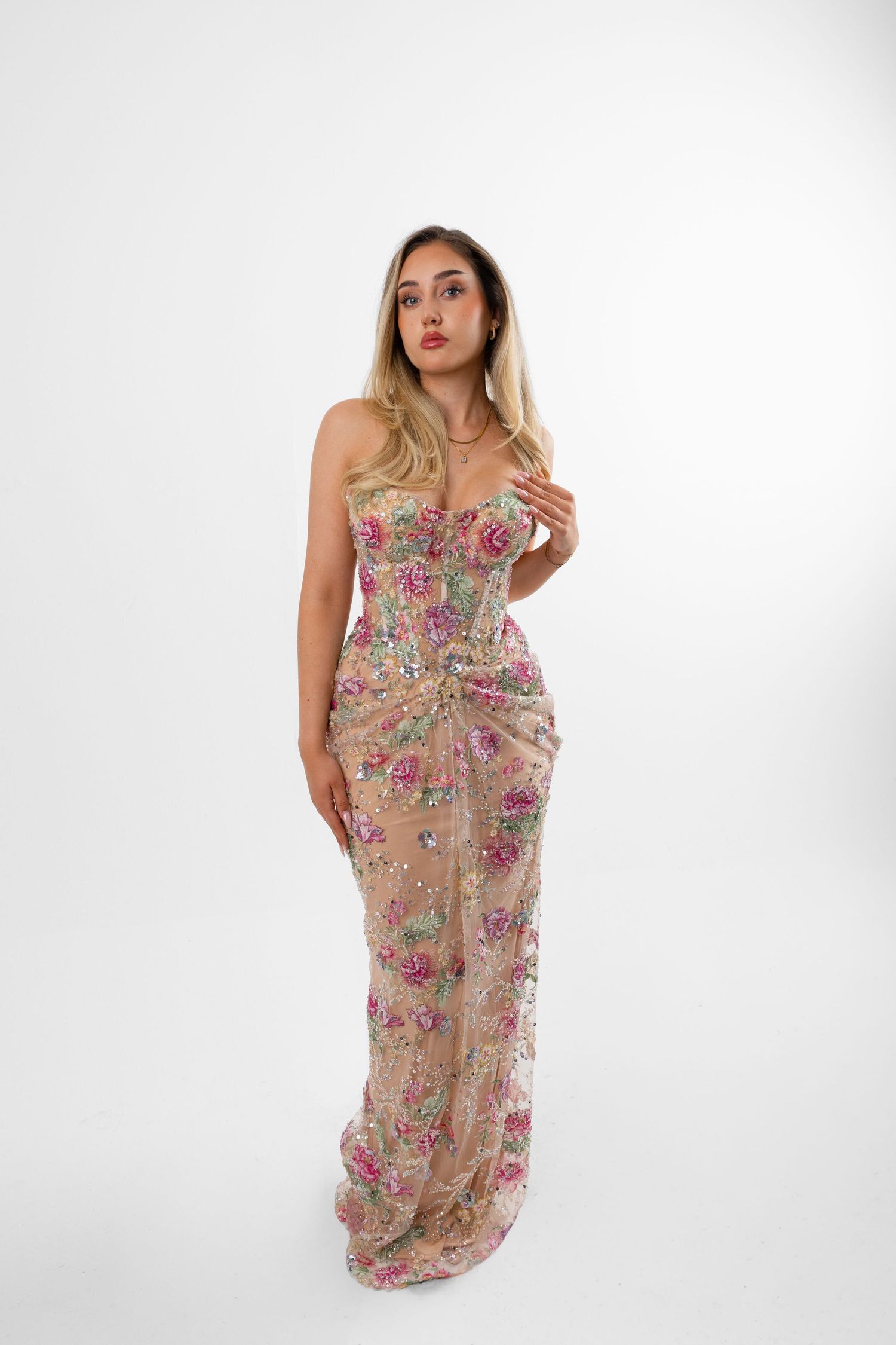 Woman wearing a strapless floral embroidered nude mesh gown with pink flowers and sequin details.