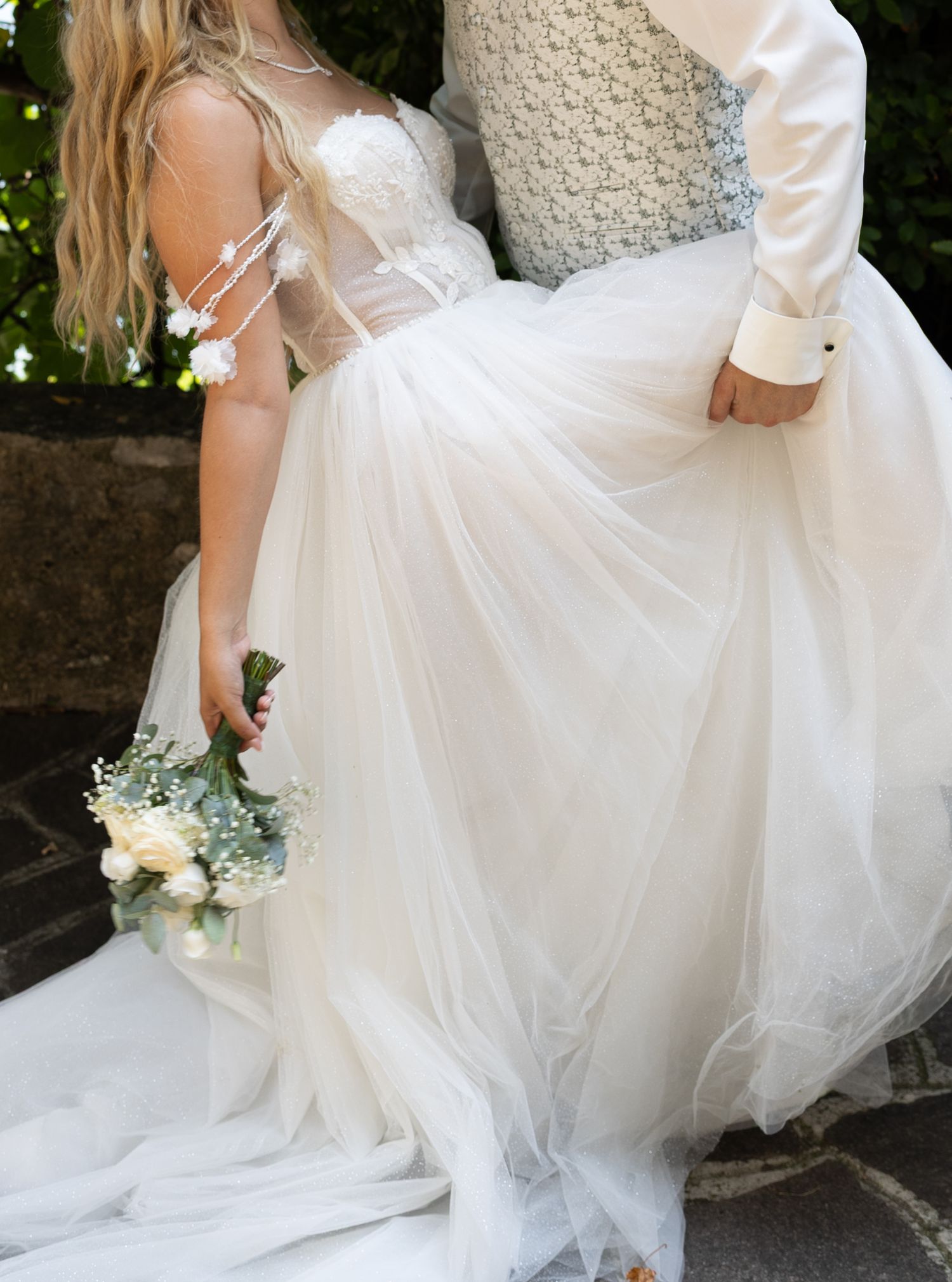 Bride in elegant white tulle ball gown holding white rose bouquet with groom at outdoor wedding.