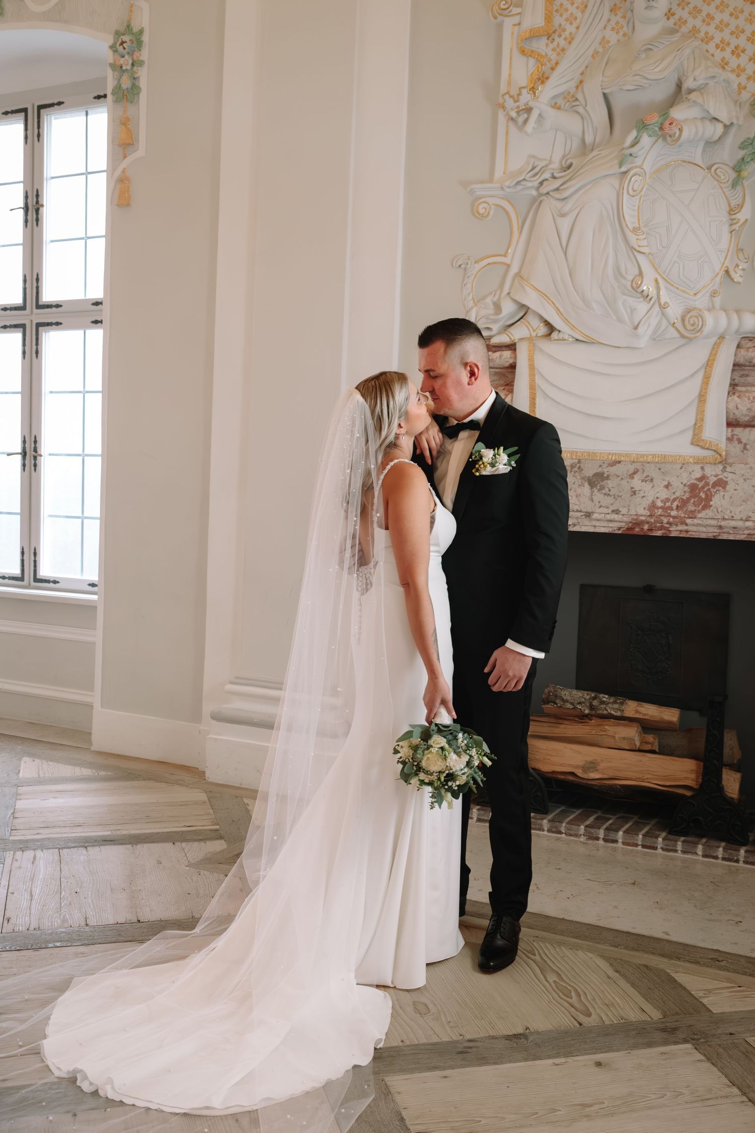 Bride and groom share a kiss in an elegant ornate room with vaulted ceilings.