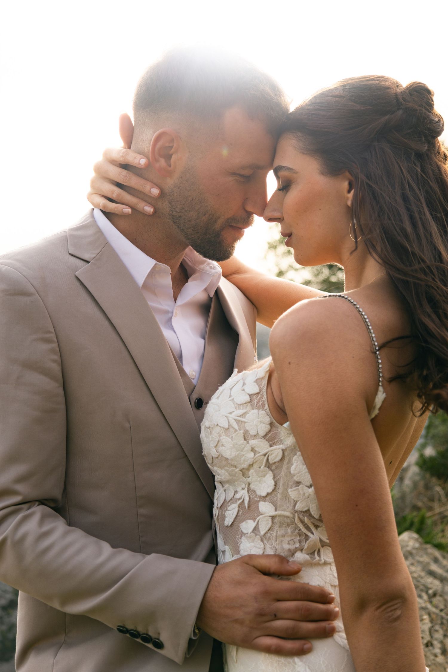 Bride and groom touching foreheads in intimate embrace with golden backlight.