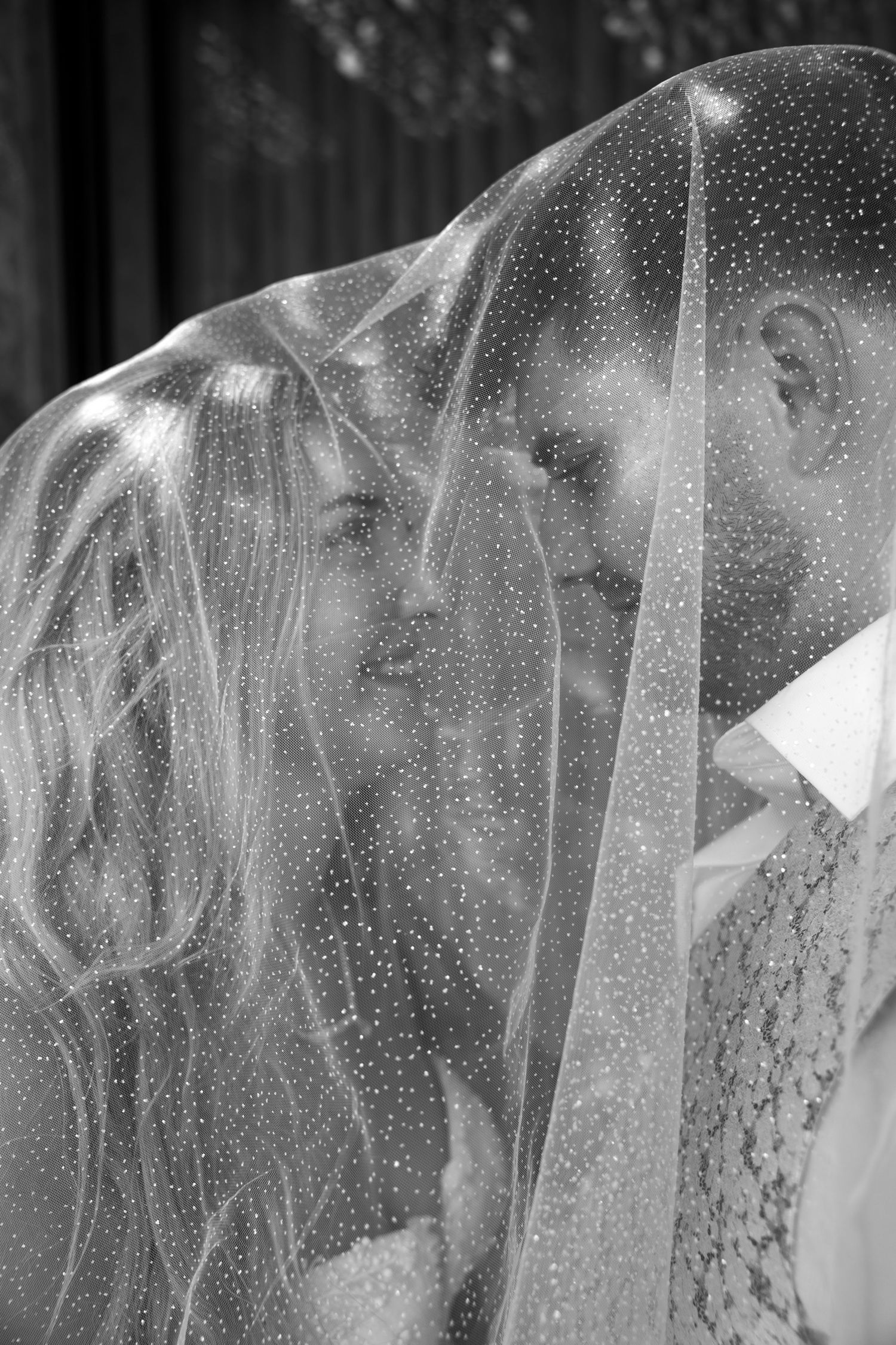 Black and white photo of bride and groom sharing intimate moment under dotted wedding veil.