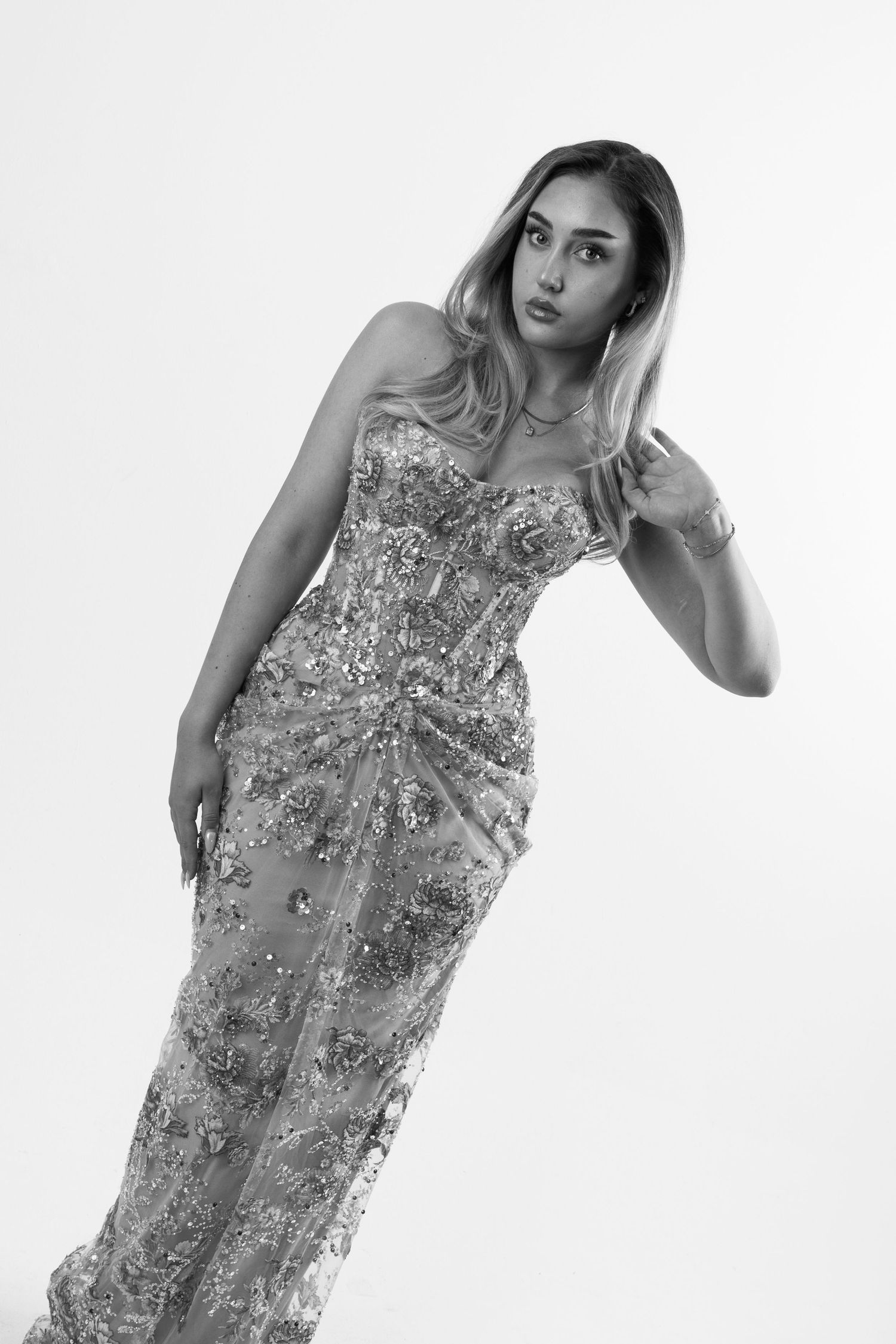 A woman poses in a sequined strapless gown, captured in black and white photography.