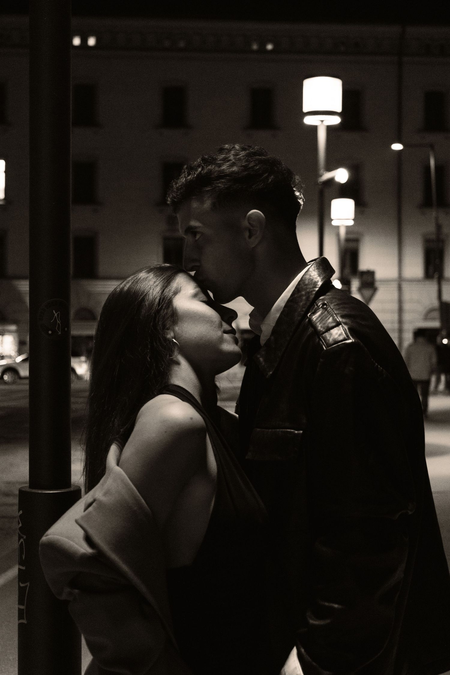 Black and white romantic couple sharing a kiss under a street lamp at night.