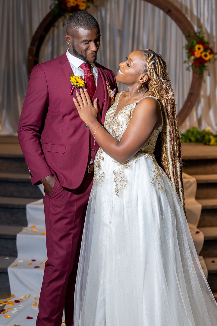 Couple poses against wooden arch backdrop with burgundy and white wedding decor.