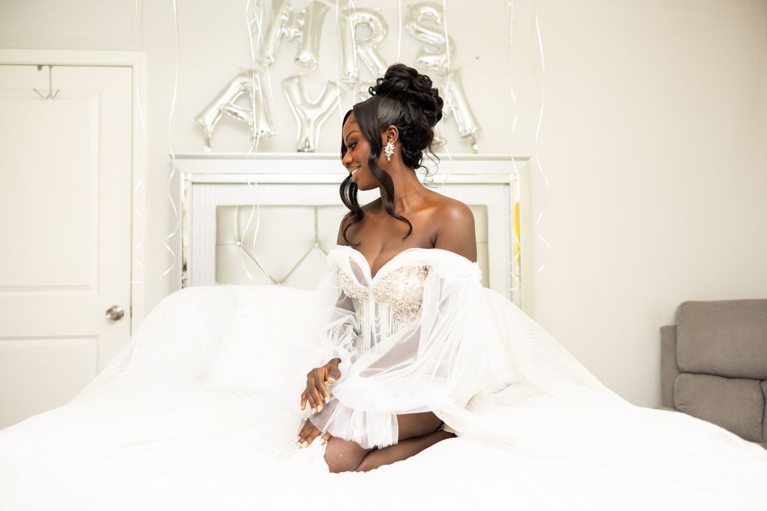 Bride in white dress poses gracefully on bed with decorative wall art.