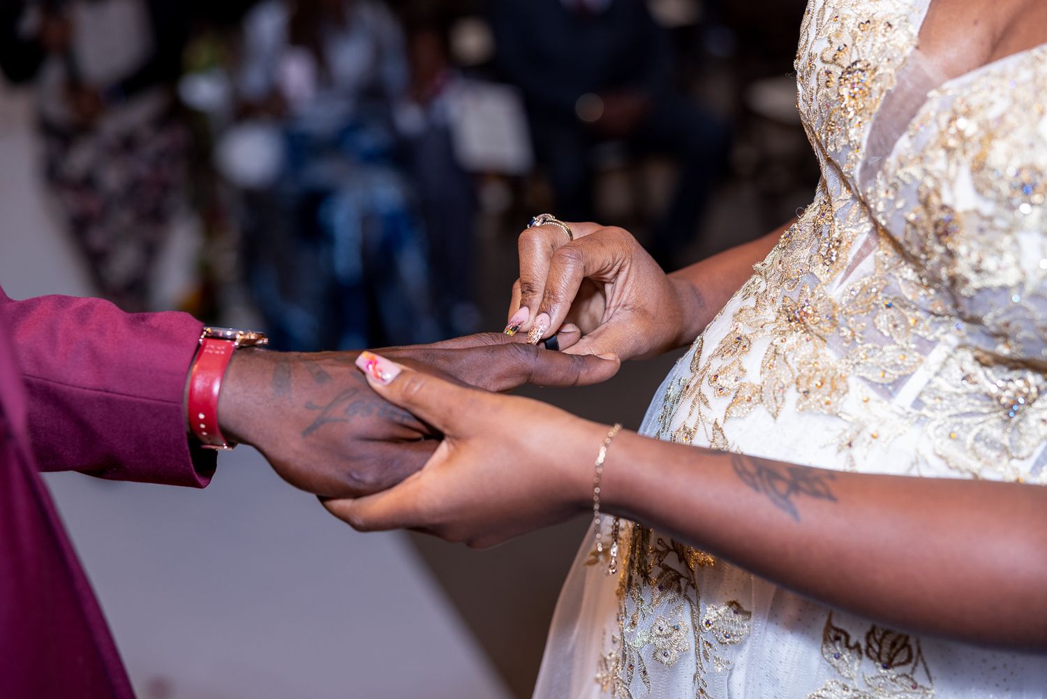 A close-up shot of hands exchanging rings during a wedding ceremony, with a white lace dress visible.