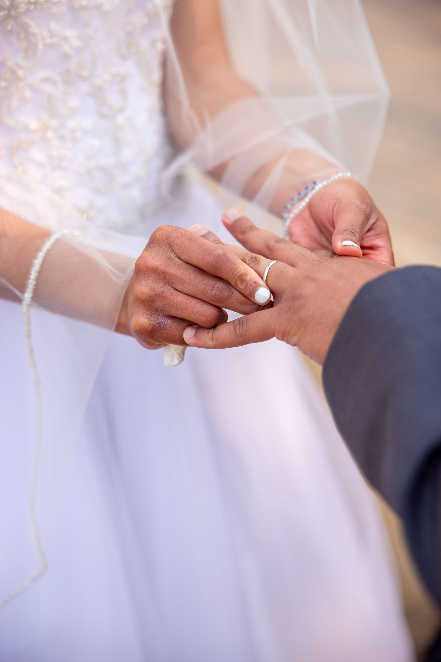 Close-up shot of hands exchanging wedding rings during an outdoor ceremony.