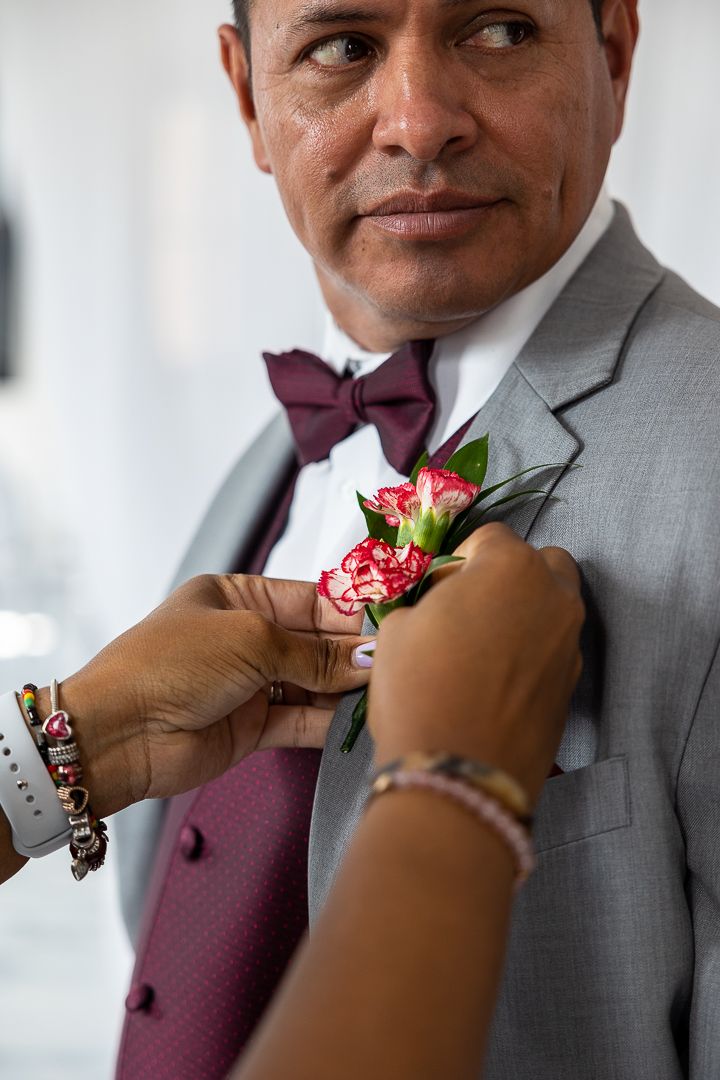 A boutonniere with pink flowers is pinned to a grey suit with burgundy tie.
