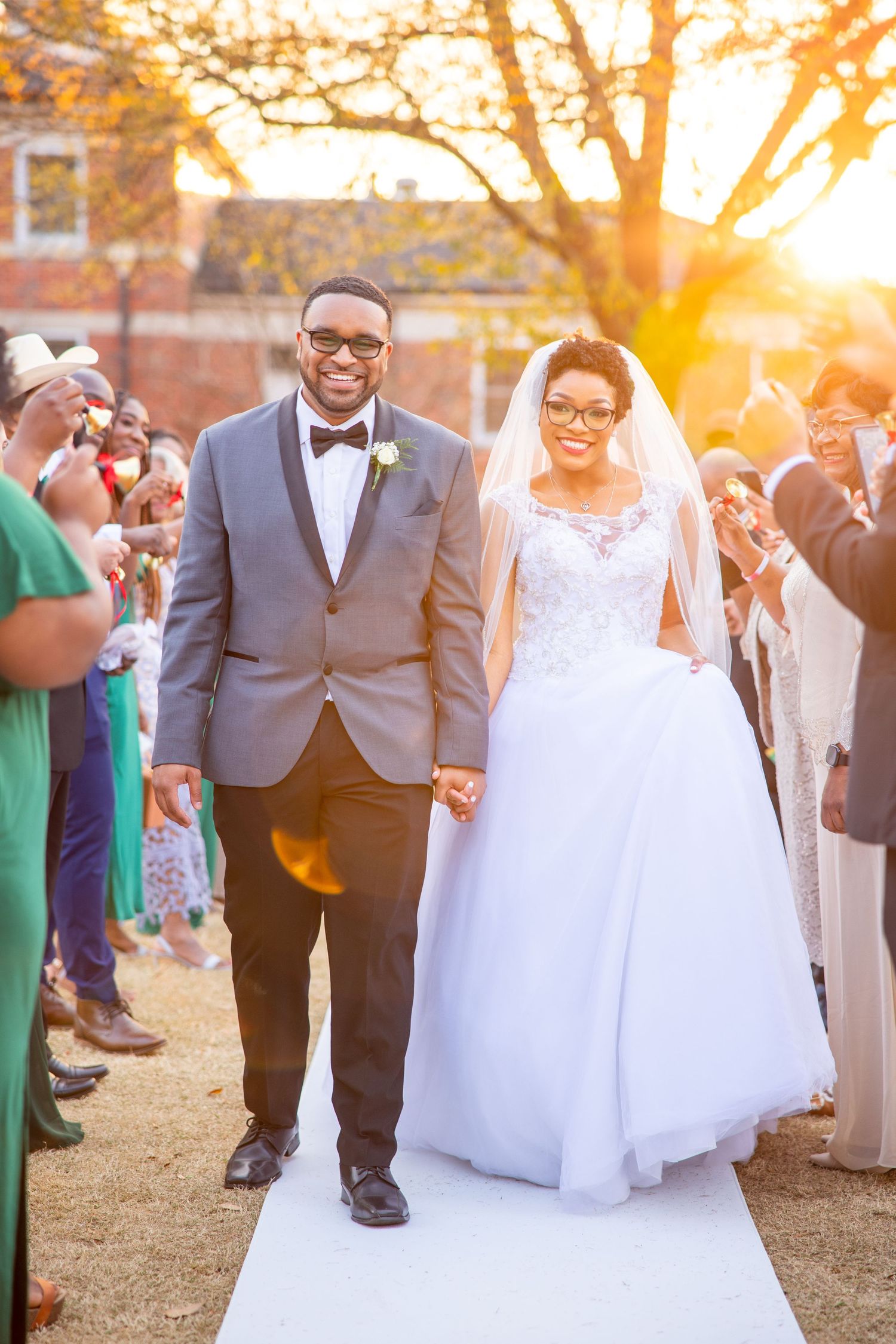 A couple walks hand in hand down a white aisle runner during their sunset wedding ceremony.