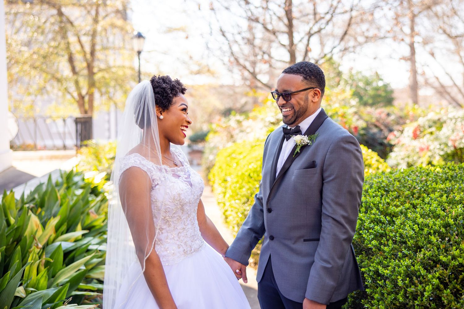 Newlyweds share candid moments during their outdoor wedding photoshoot near manicured hedges.