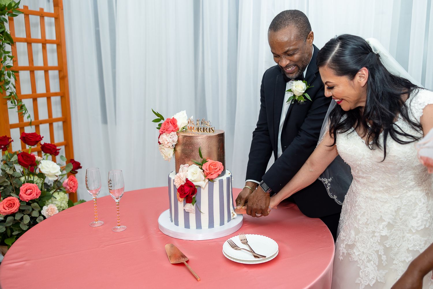 Bride and groom cut their modern striped wedding cake decorated with red flowers.